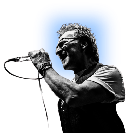 A man singing into a microphone with a blue background, wearing sunglasses and a tactical vest.