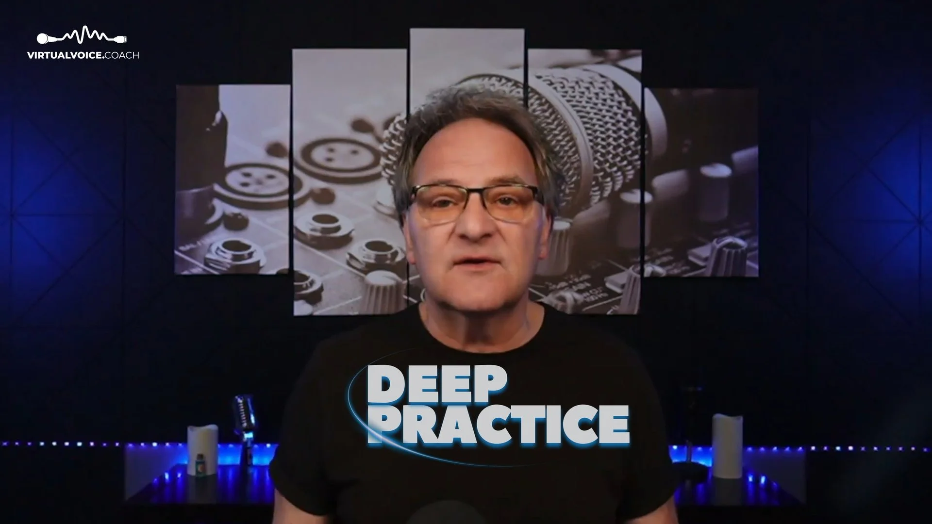 A man wearing glasses and a black shirt with the words 'Deep Practice' printed on it, standing in front of a digital background with an image of a microphone and buttons, in a dark room with blue LED lighting.