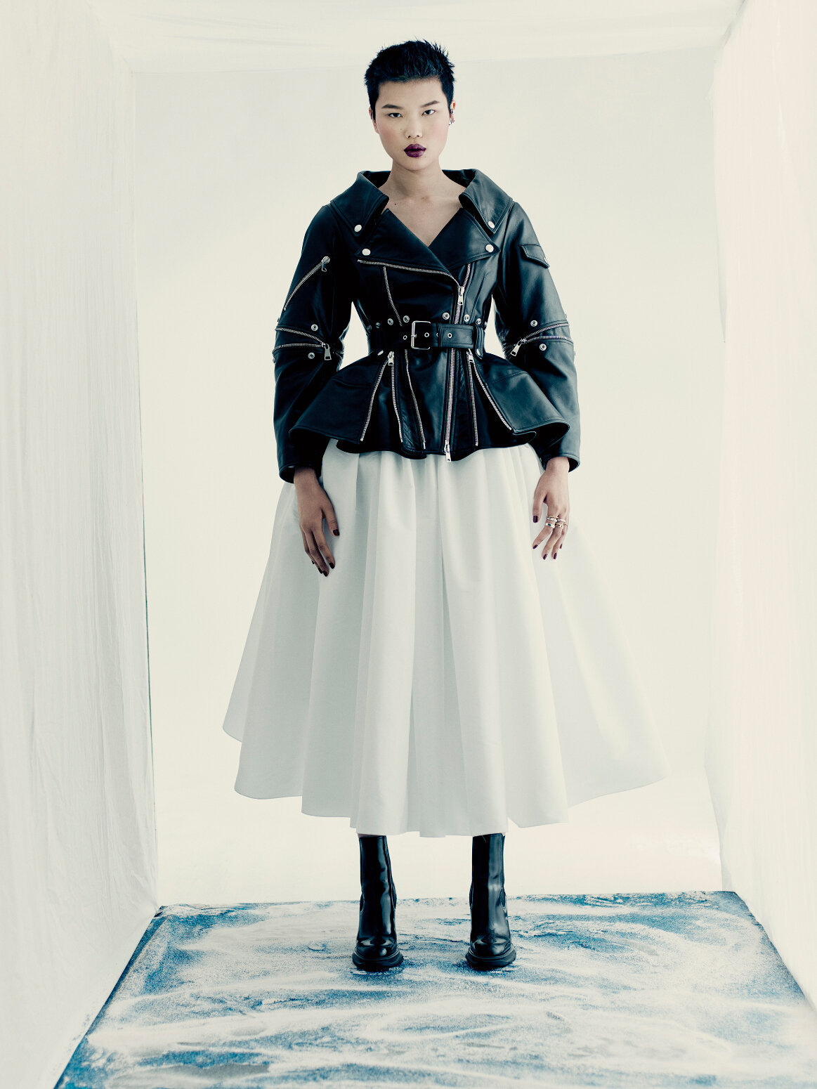  A biker jacket with an open neckline and multi-zip exploded peplum in black leather and a full gathered skirt with dropped pocket detailing in white poly faille.  
