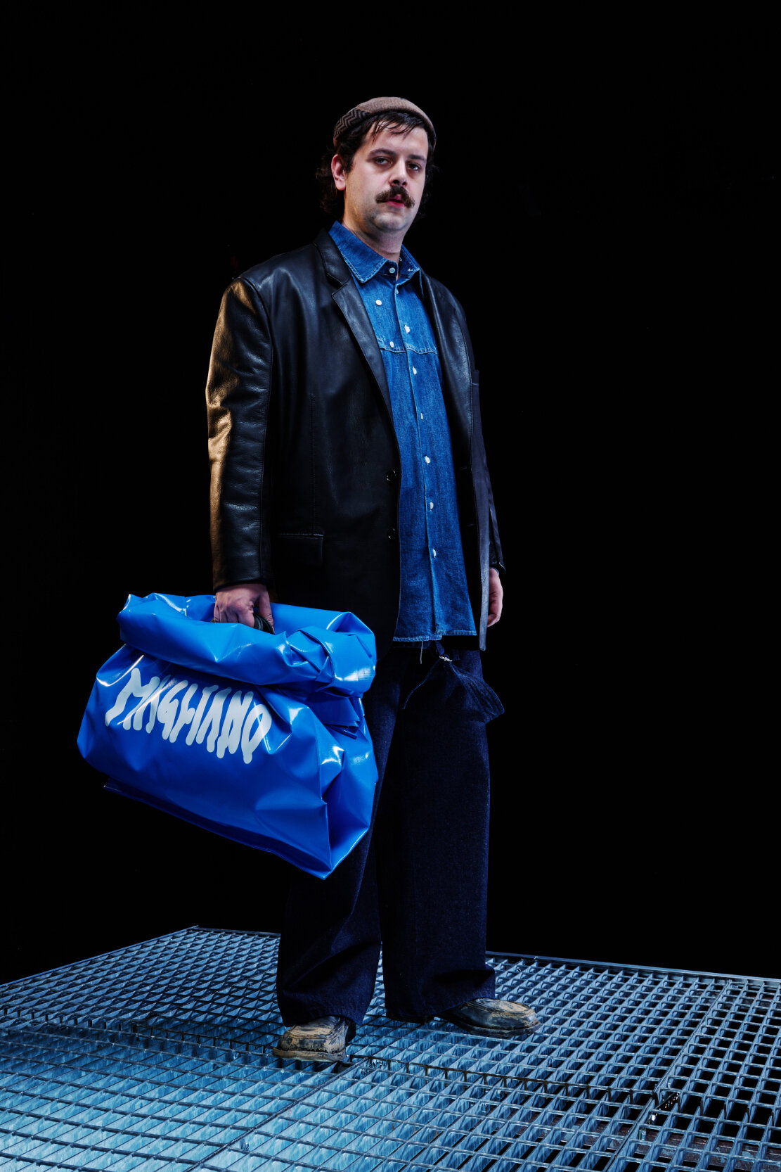  Model wears blue shirt under leather jacket and holds a large blue bag for Magliano's Spring/Summer 2022 collection for Milan Fashion Week. 