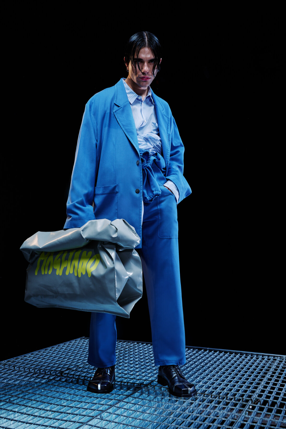  Model wears blue suit and holds large green bag for Magliano's Spring/Summer 2022 collection for Milan Fashion Week. 