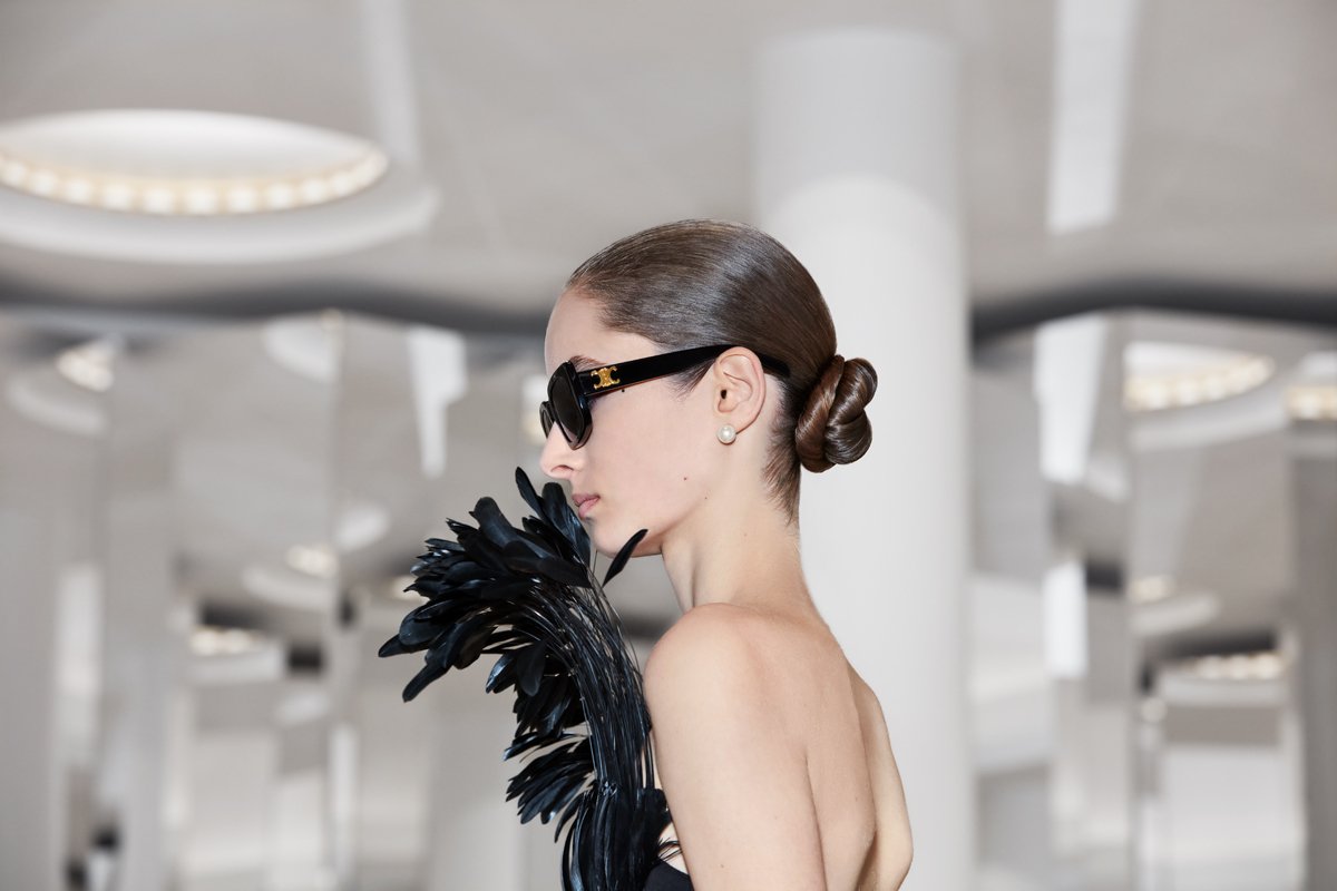  model standing profile closeup of face wearing black sunglasses with black feathers in front of face 