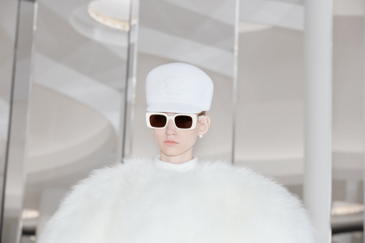  white cap with Celine triomphe logo, white rimmed acetate sunglasses and white ball-shaped fur dress. 