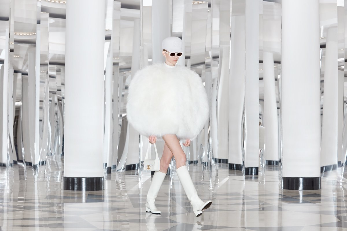  white cap with Celine triomphe logo, white rimmed acetate sunglasses, white ball-shaped fur dress and white knee-high boots. 