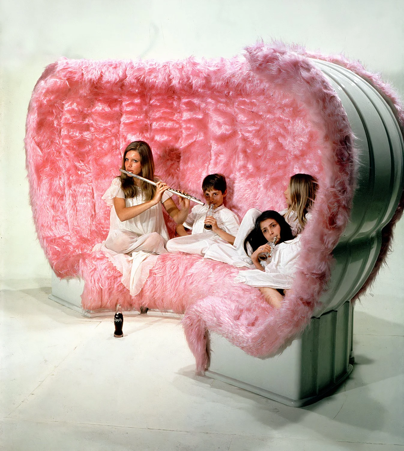 Four people sitting on a large pink couch, drinking and playing the flute