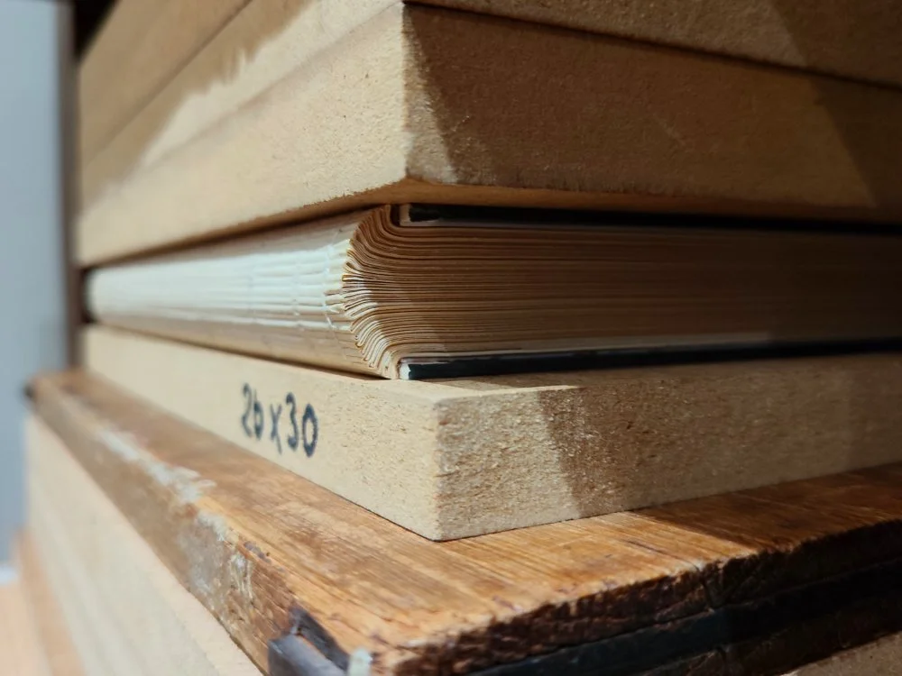 Vue sur le dos et la tranche d'un livre en presse de corps d'ouvrage. On peut voir le travail du dos, l'endossure et la création des mors pour loger les cartons.