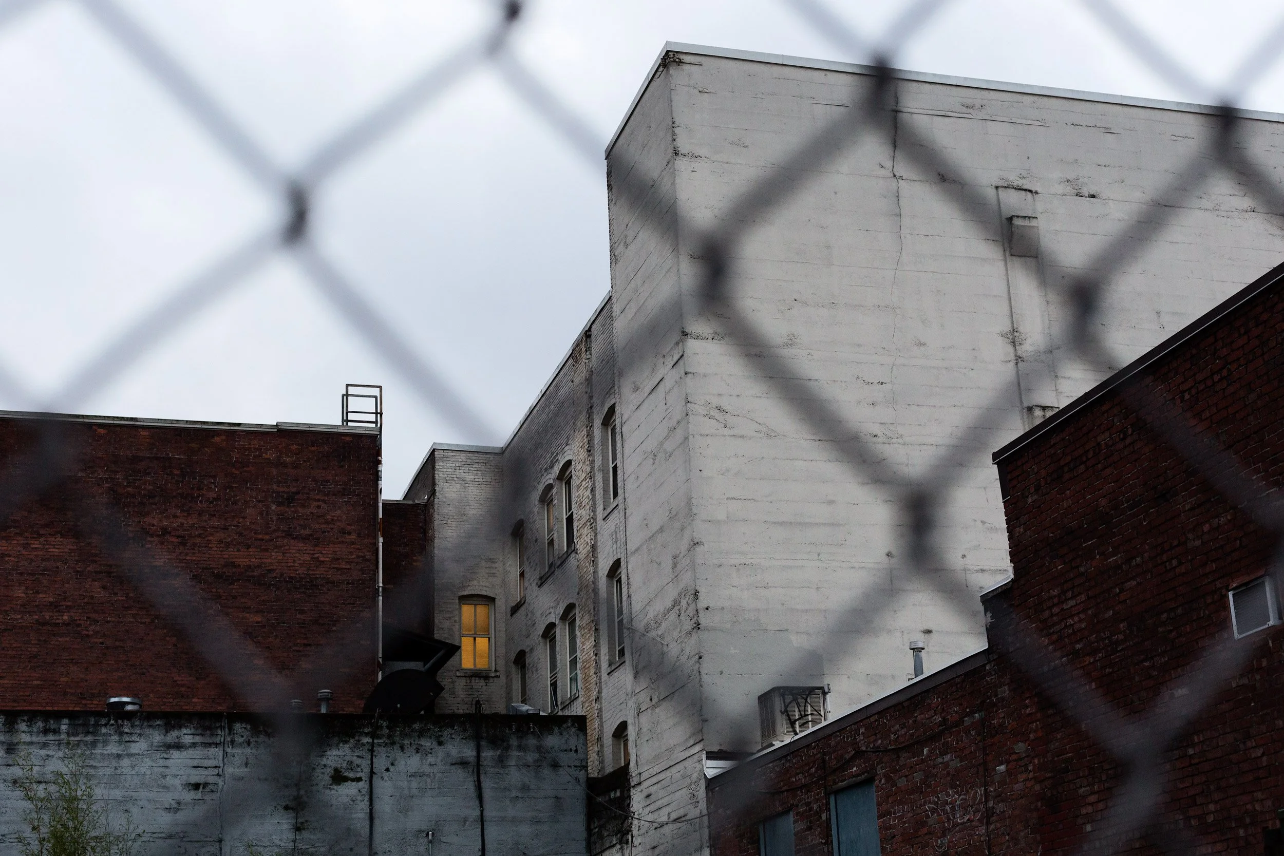 buildings-and-yellow-lit-window-through-a-chain-link-fence-.jpg