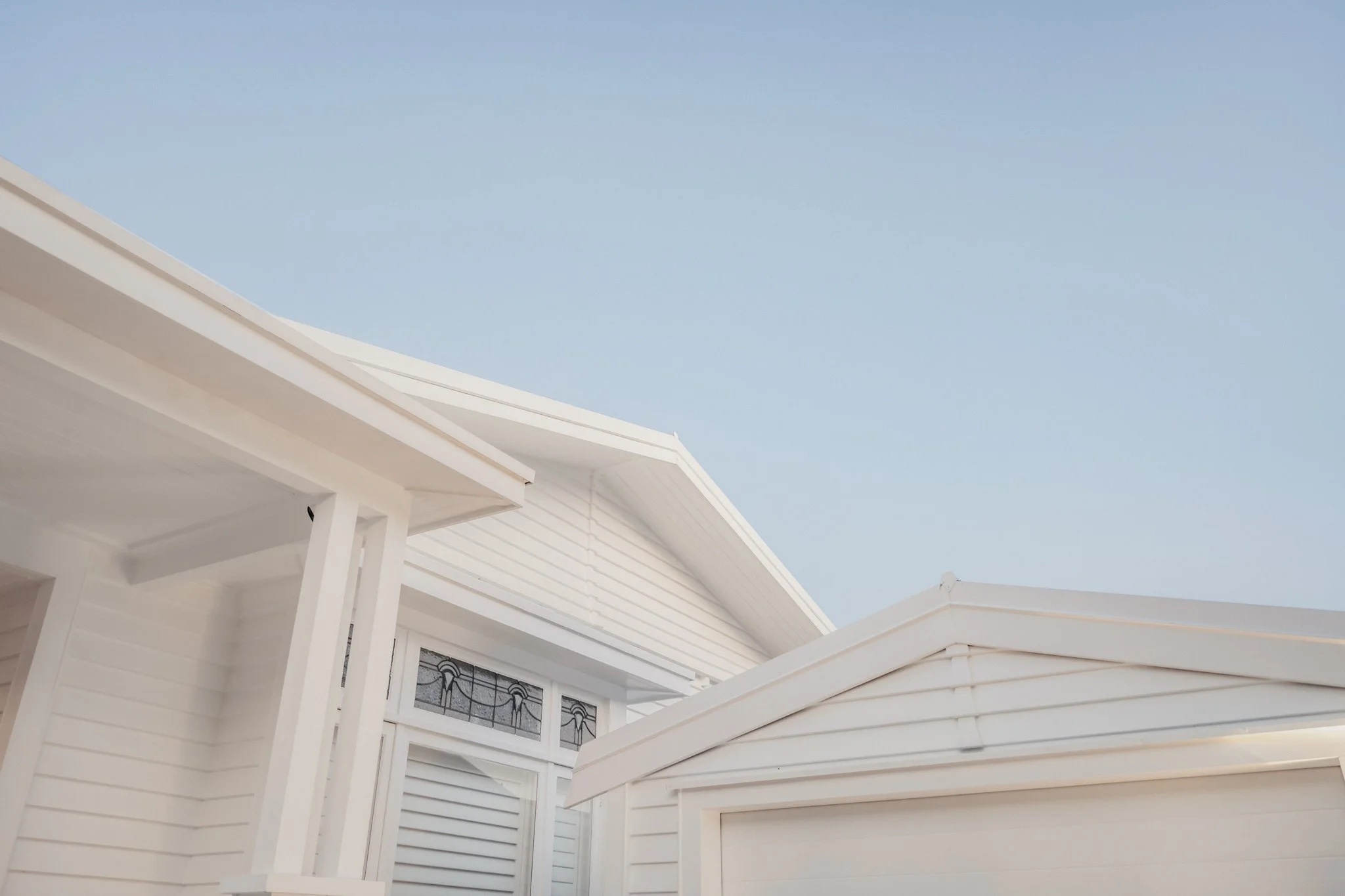 Gable and porch detail of the Point Chevalier Transitional Bungalow by Macfie Architecture, with white weatherboard cladding, exposed eaves and original leadlight windows
