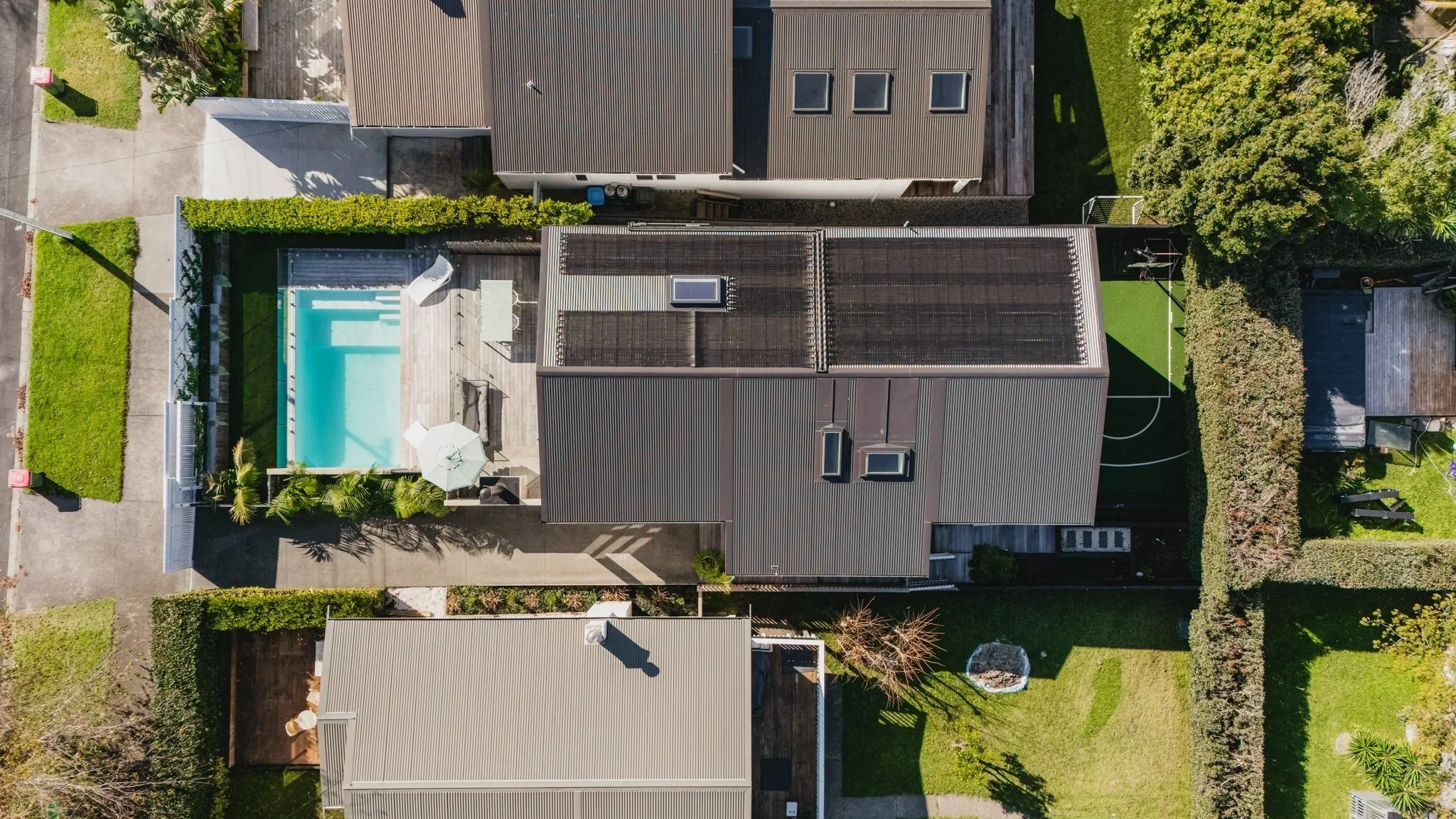 Aerial view of a new build bungalow in Westmere, Auckland, showing the north-facing pool and entertaining terrace to the west and a bespoke sports court to the east, set within a residential neighbourhood.