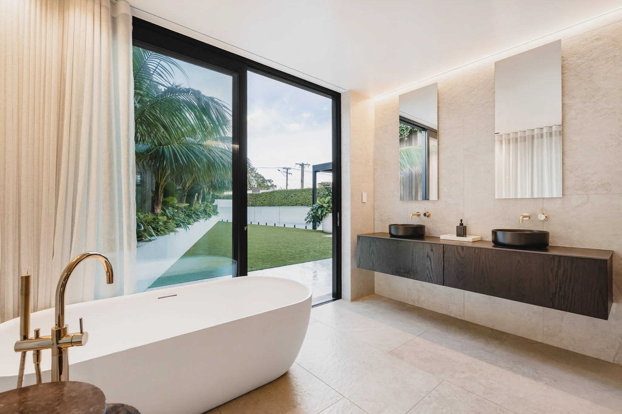 Bespoke new-build property with spa like bathroom, soft ambient LED lighting frames the natural stone bathroom with a neutral palette and dark oak cabinetry and polished brass accents.