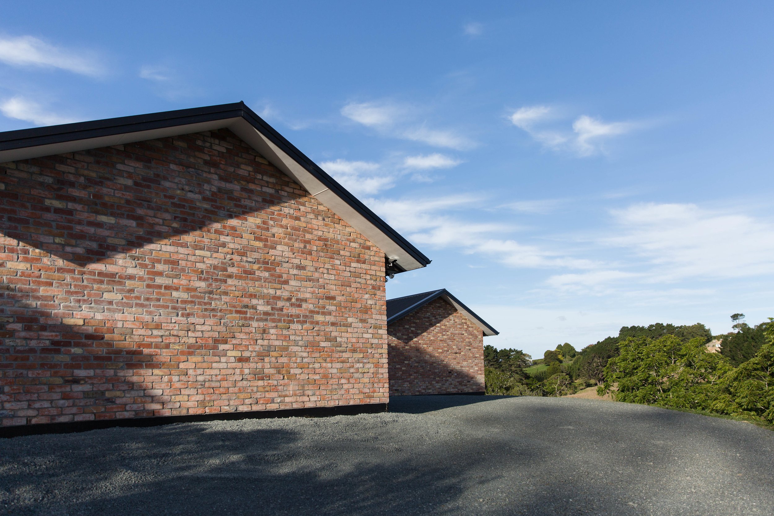Whitford House recycled brick gable ends seen from the gravel driveway, with the Whitford valley beyond