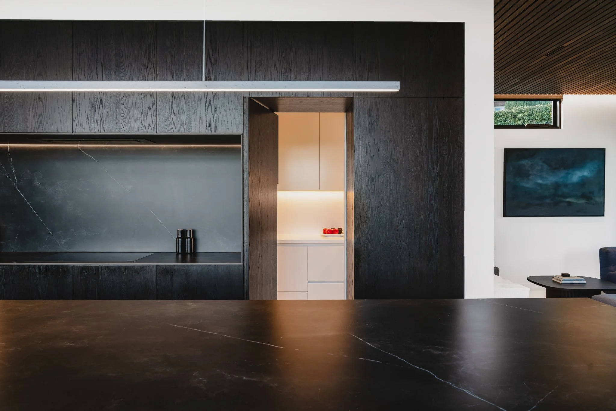 Bespoke new-build design with designer kitchen dark stone bench running the full length of the room, with blackened oak cabinetry below and a concealed scullery behind and a pendant.