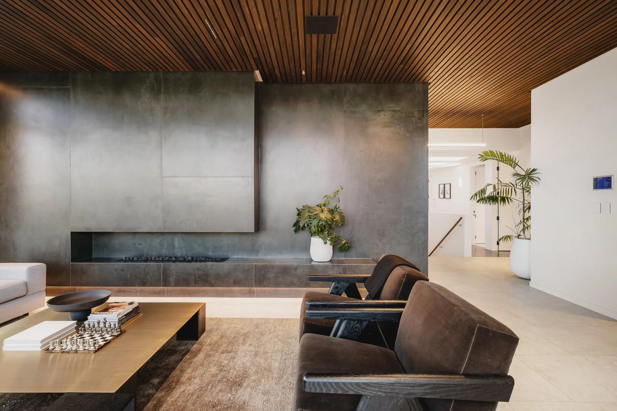 St Heliers New-Build — open plan living room with patinated steel fireplace wall, timber slat ceiling, velvet armchairs and brass coffee table, interiors by Macfie Architecture Auckland