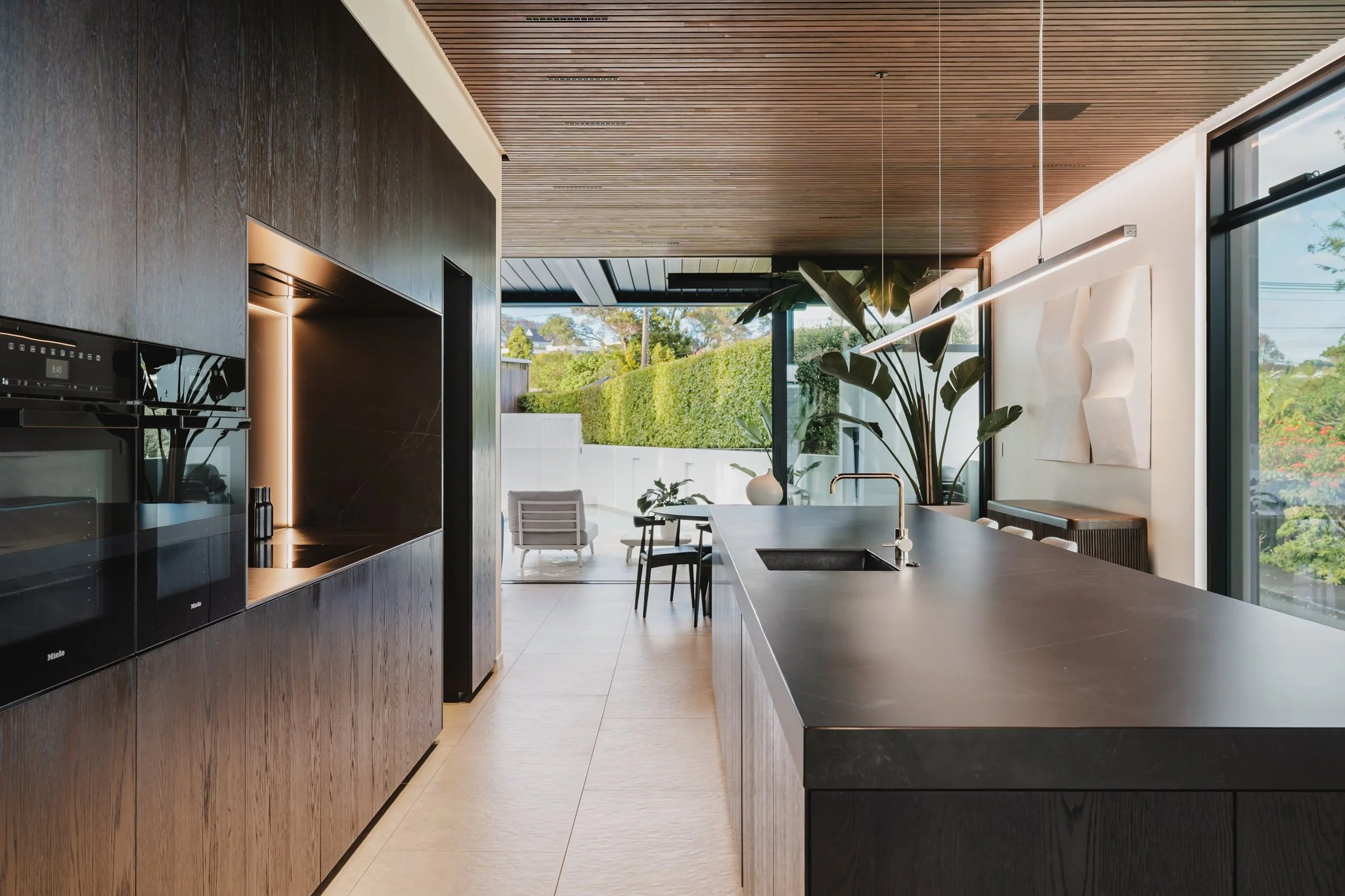 Bespoke new-build design with designer kitchen dark stone bench running the full length of the room, with blackened oak cabinetry below and a concealed scullery behind and a pendant.