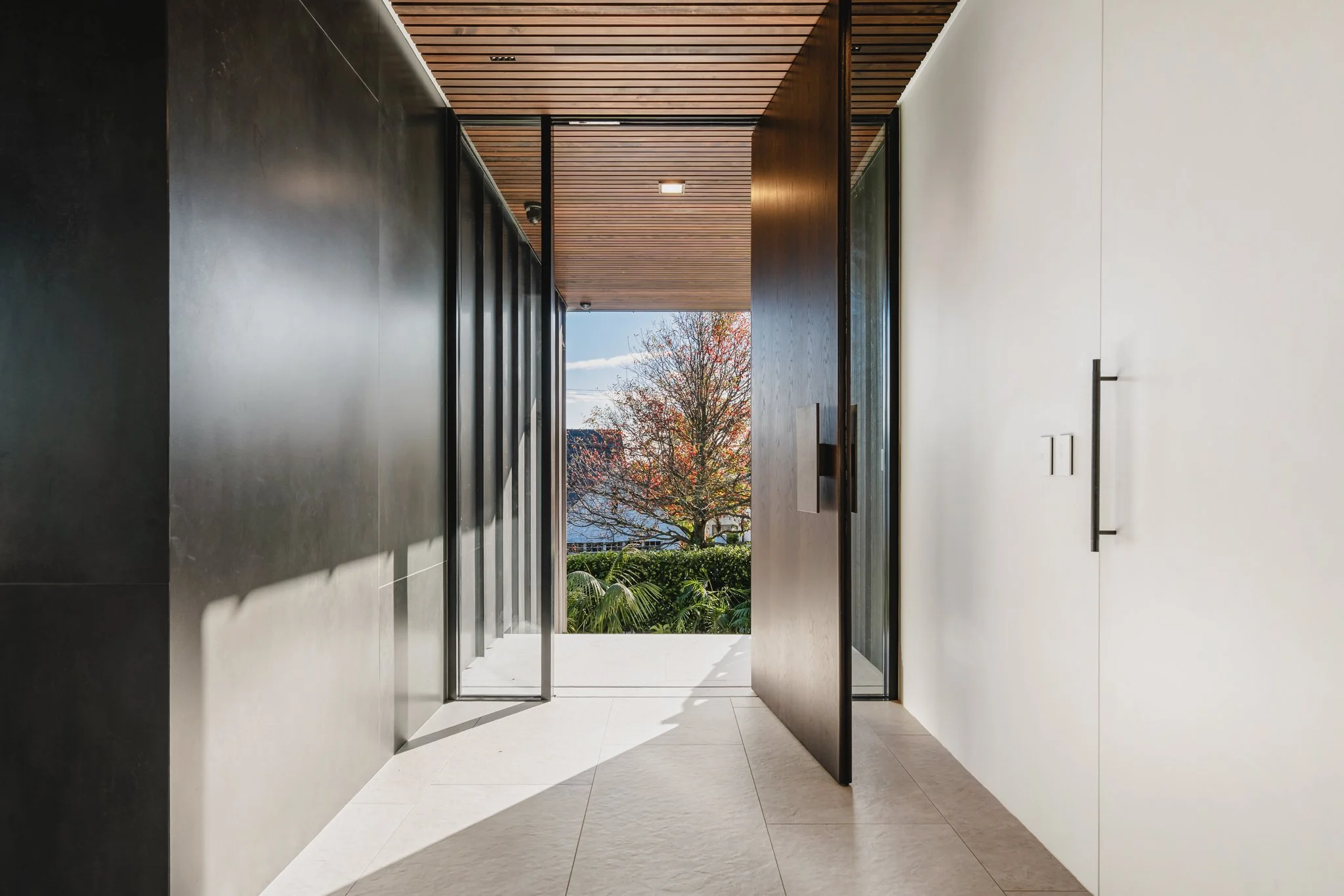 Bespoke new-build in collaboration with Onform construction - large format front door with copper and wood panel accents, stone floor in entrance way and Xanthe White Garden.