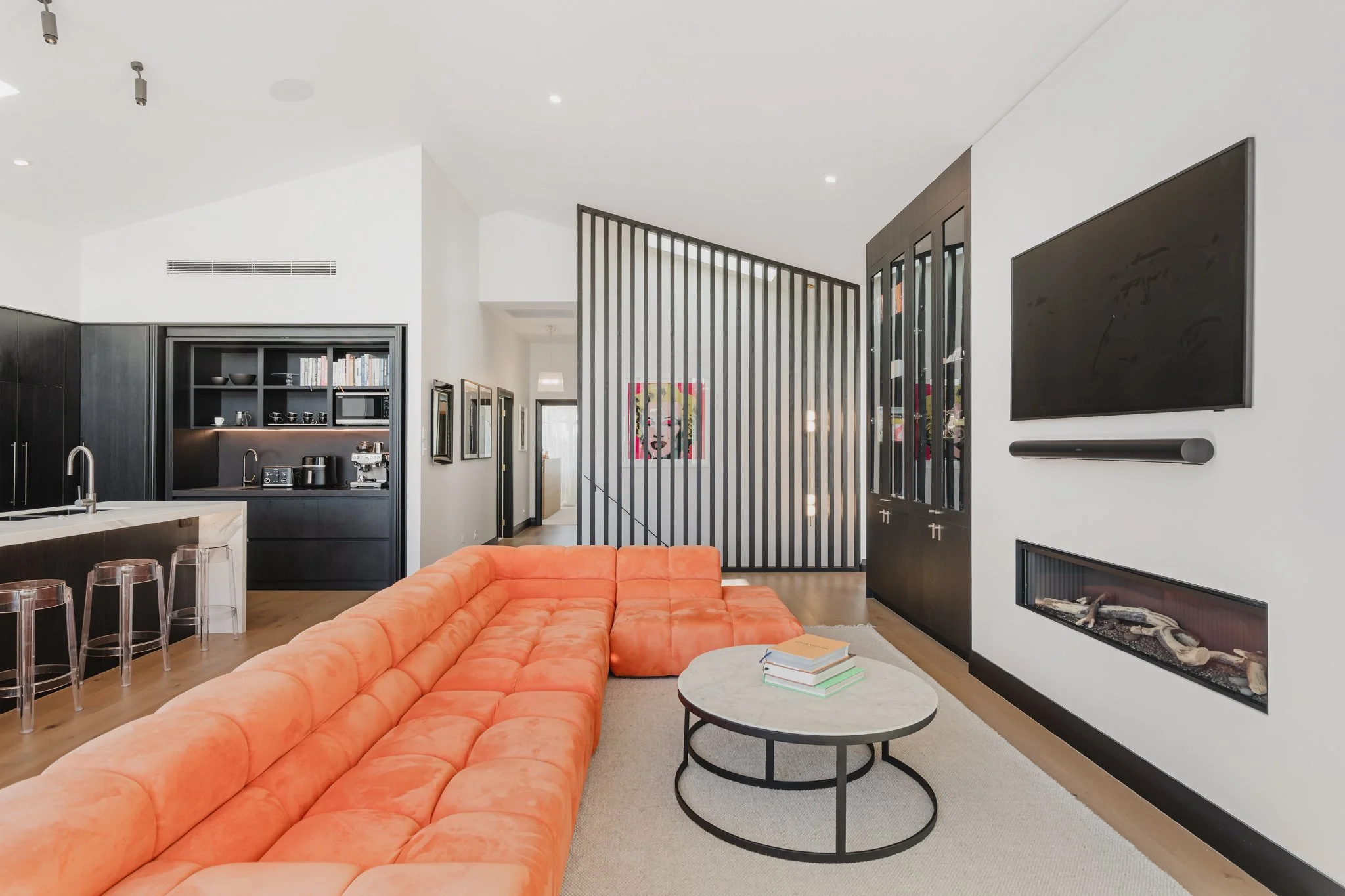 Open plan living room with linear gas fireplace, orange sectional sofa and black batten stair screen in a new build Auckland bungalow, Westmere.