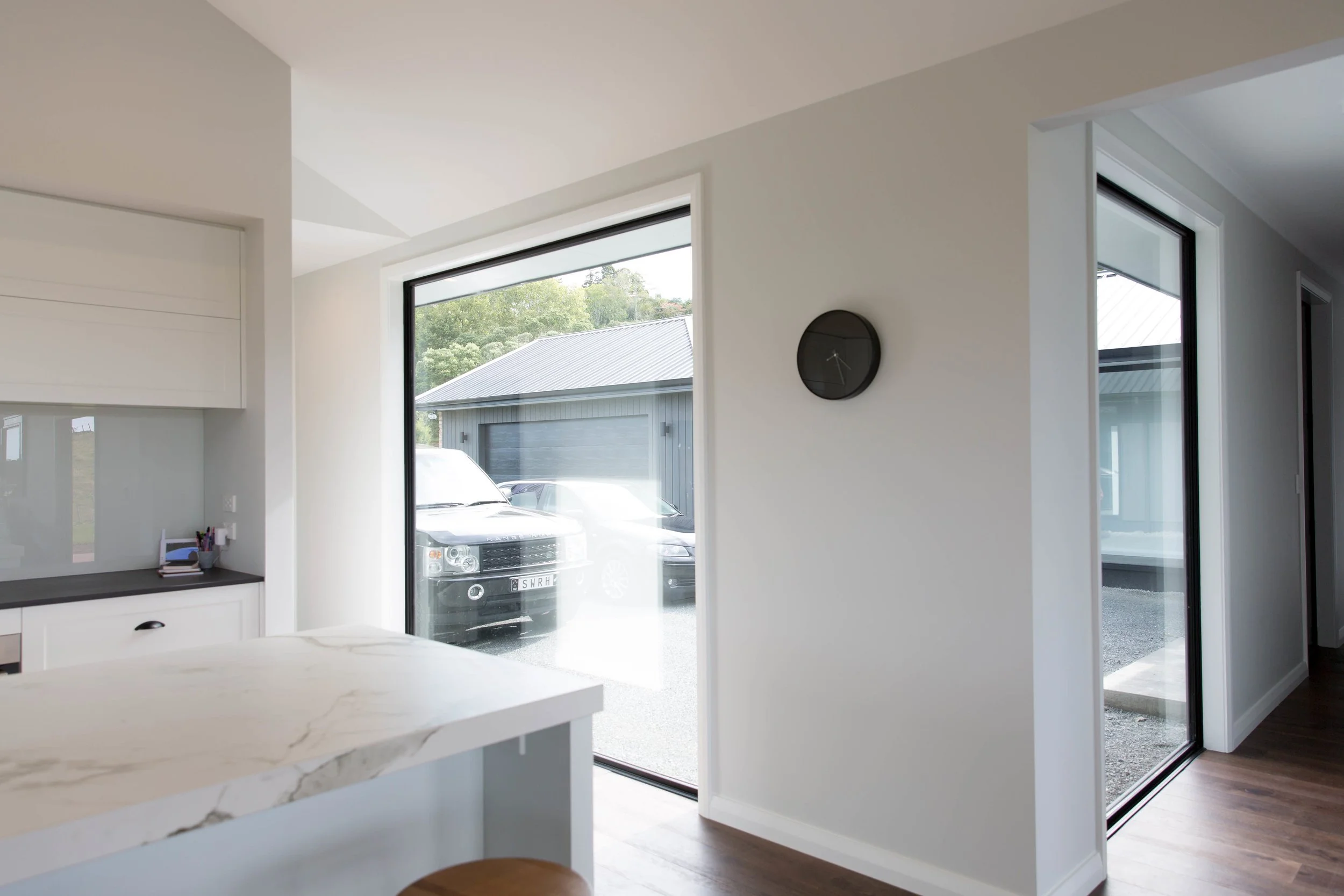 Whitford new-build kitchen with stone island bench and built-in study nook, looking through a picture window to the detached garage