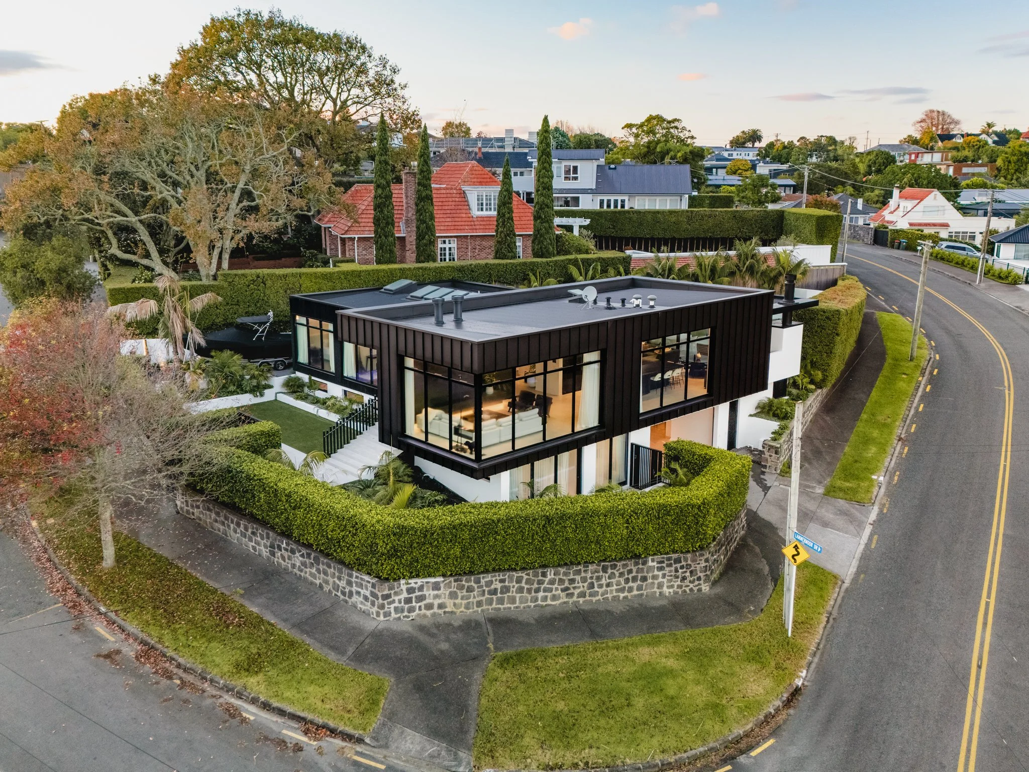 Bespoke New-Build design by Macfie Architecture - featuring A dark vertical seam metal upper volume sits above a white rendered base, anchored to the street by a heritage basalt stone wall and gardens by Xanthe White.
