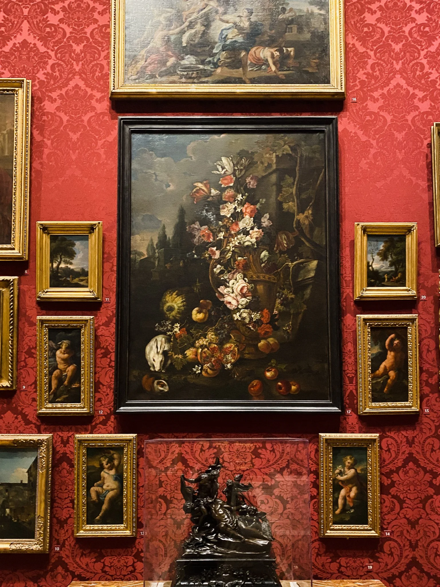 A gallery wall at the Walters Art Museum featuring a large floral painting with a rabbit surrounded by smaller paintings of landscapes and cherubs