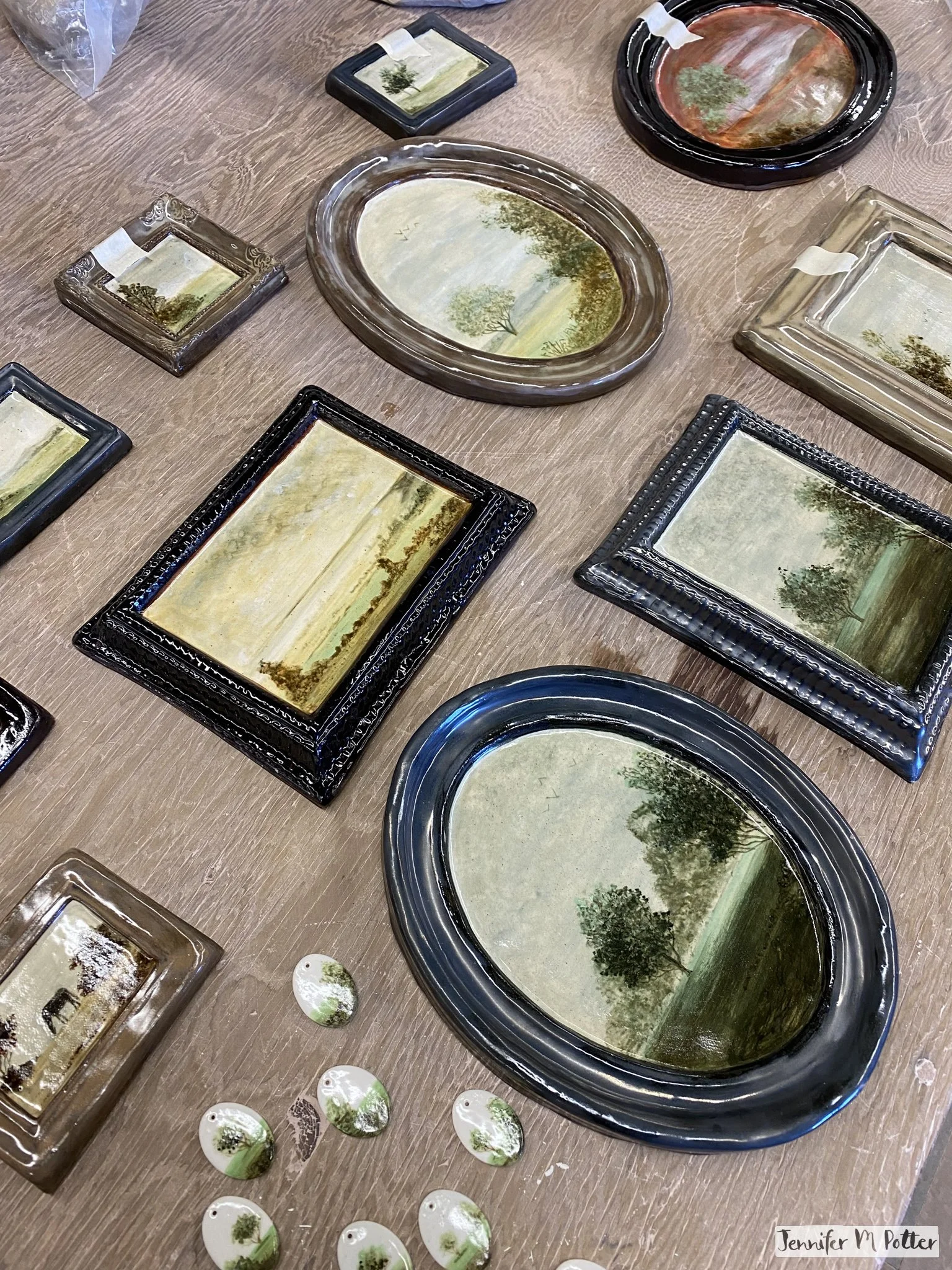 Glazed and fired ceramic paintings laid out on a work table. One painting is messier and very red compared to the others.
