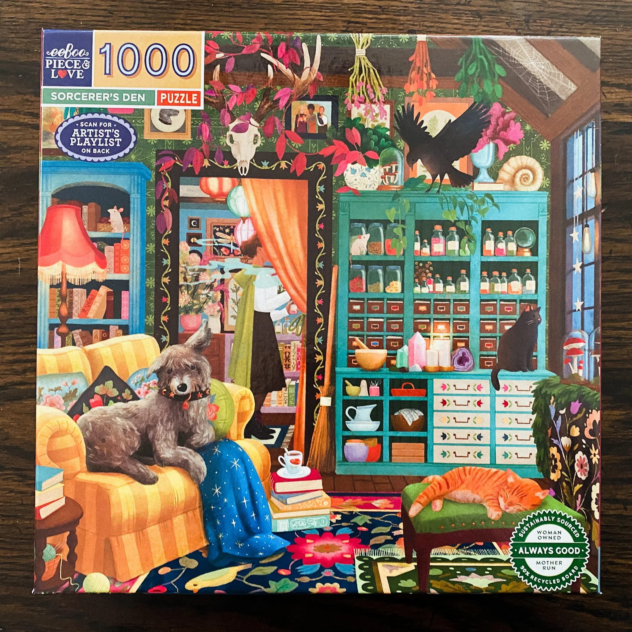 Sorcerer's Den 1000-piece puzzle box by eeBoo, illustrated by Jennifer M Potter, featuring cozy magical den with Irish Wolfhound on yellow striped loveseat, orange cat on green cushion, turquoise apothecary cabinet, hanging dried flowers, and raven