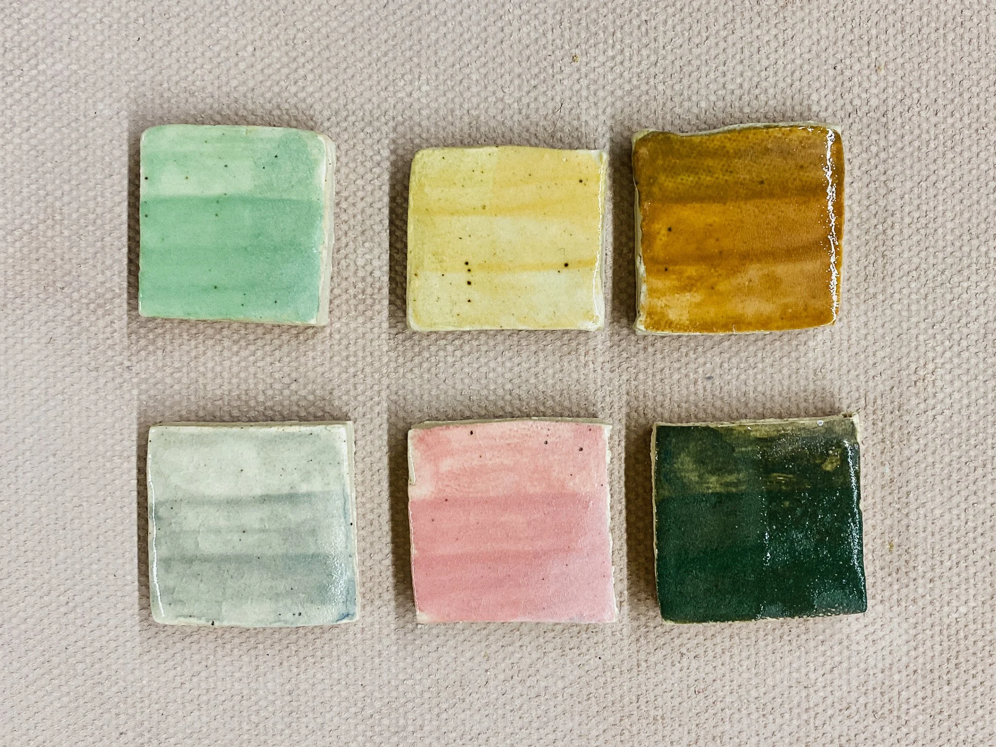 Six colorful test tiles in pistachio, straw, light brown, pearl gray, blush, and dark green