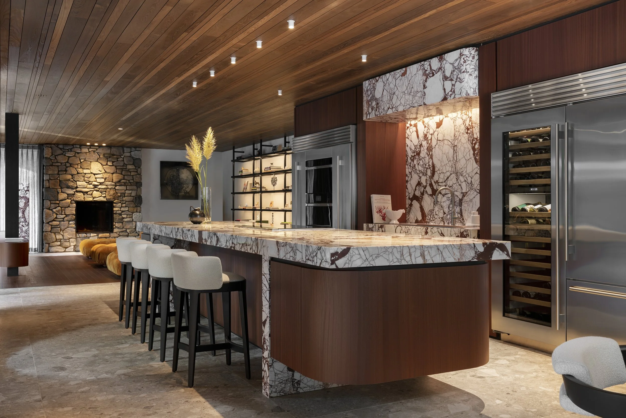 Modern kitchen with marble island, wooden ceiling, stone fireplace, Subzero & wolf appliances, and Molteni&C bar stools.
