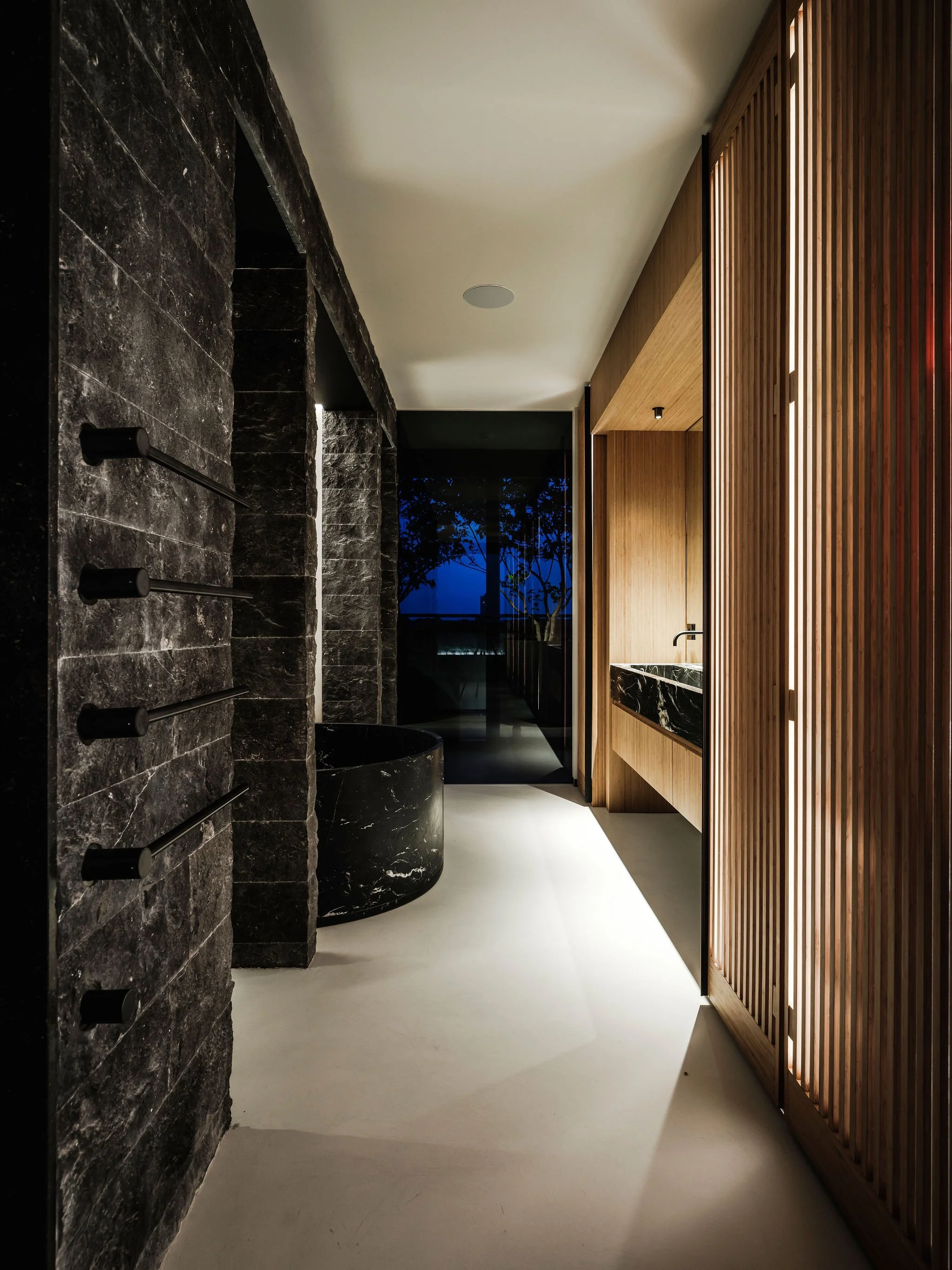 Custom  bathroom interior with black marble elements, wooden slats, and a free-standing black marble Agape bathtub visible in the background.