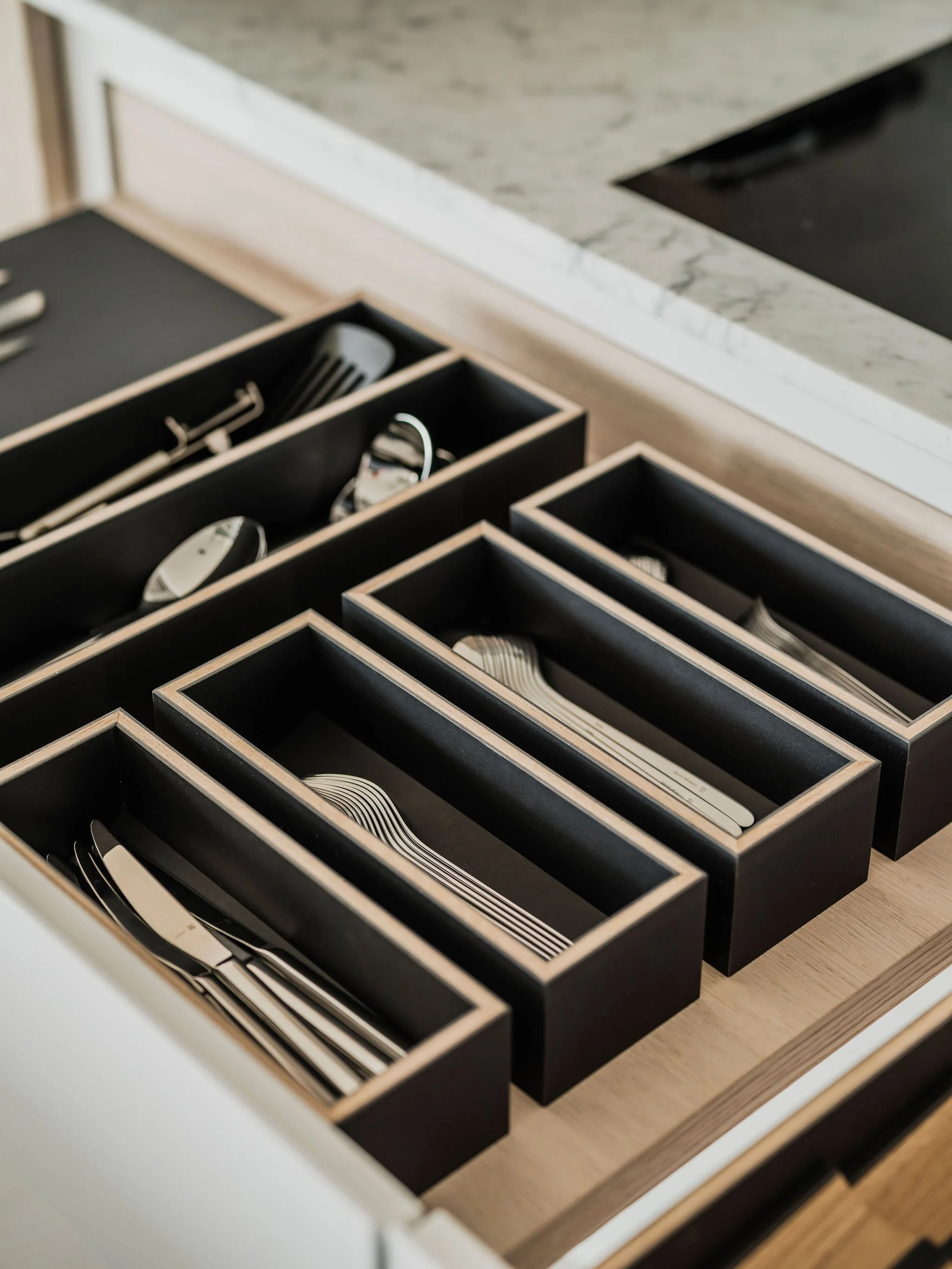 Bespoke organised black compartments with cutlery, utensils, in a kitchen drawer.