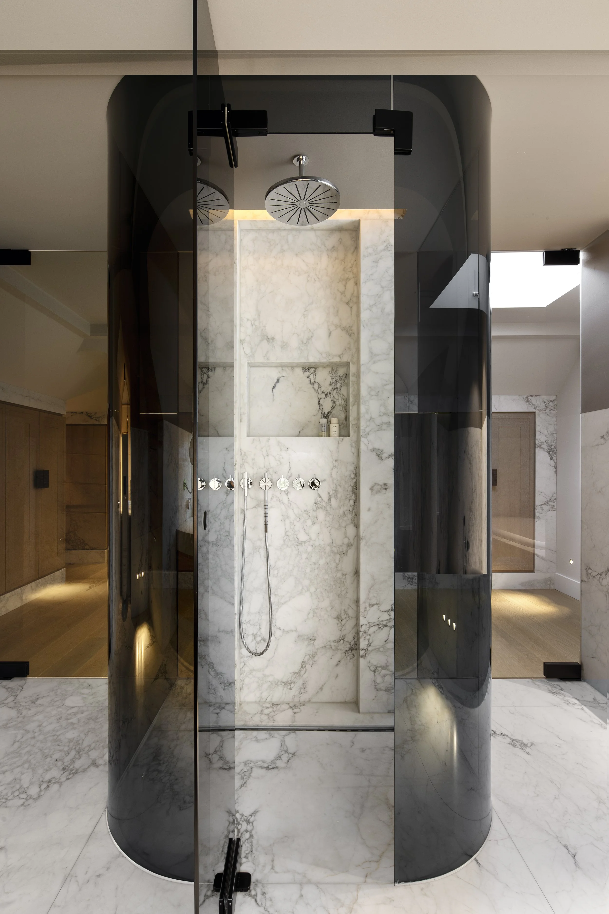 Design shower with marble walls and floor, black and dark gray curved glass panels, and a rain showerhead ceiling.