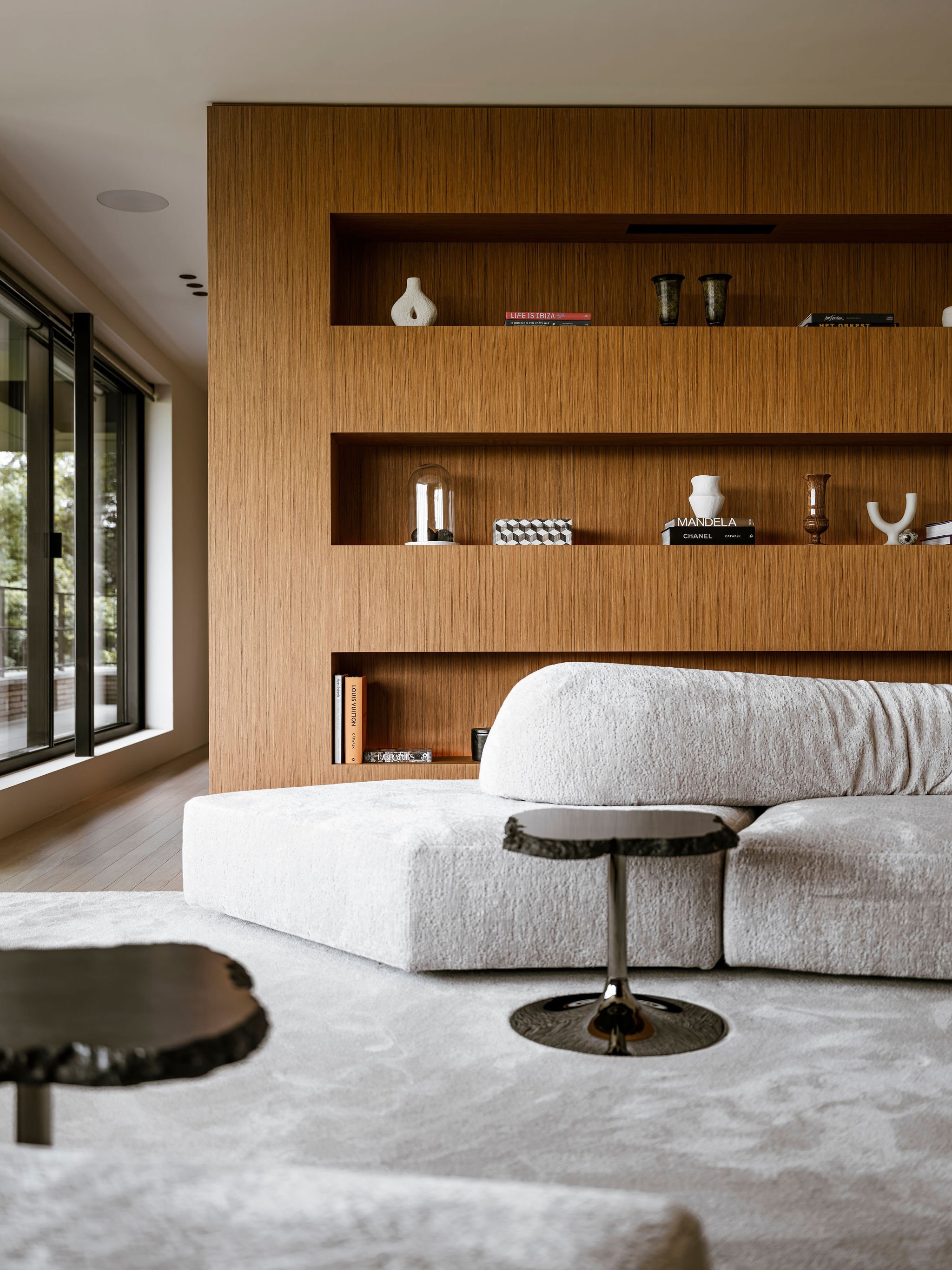 Living room with bespoke built-in teak wooden shelves, white textured Edra sofa, and black stone Edra side tables.