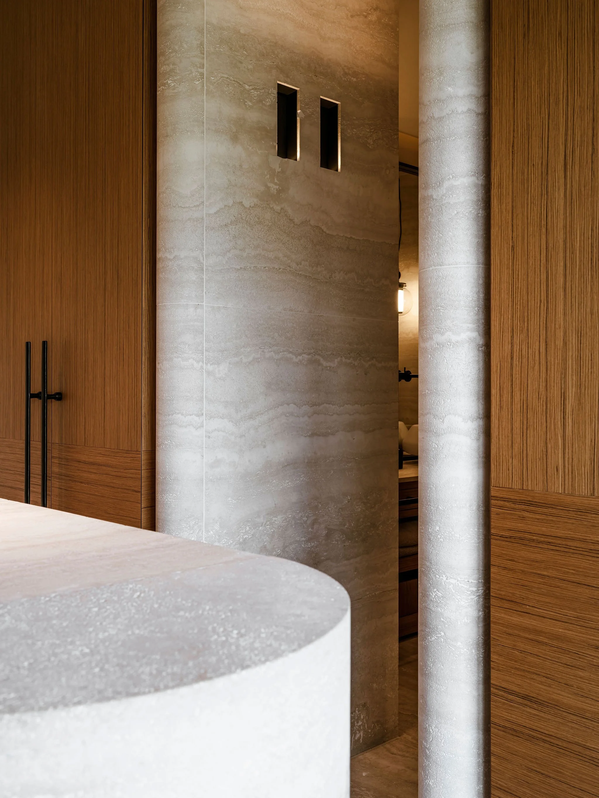 Interior view of a walk in closet with beveled travertine, teak wooden cabinets, and lighting.