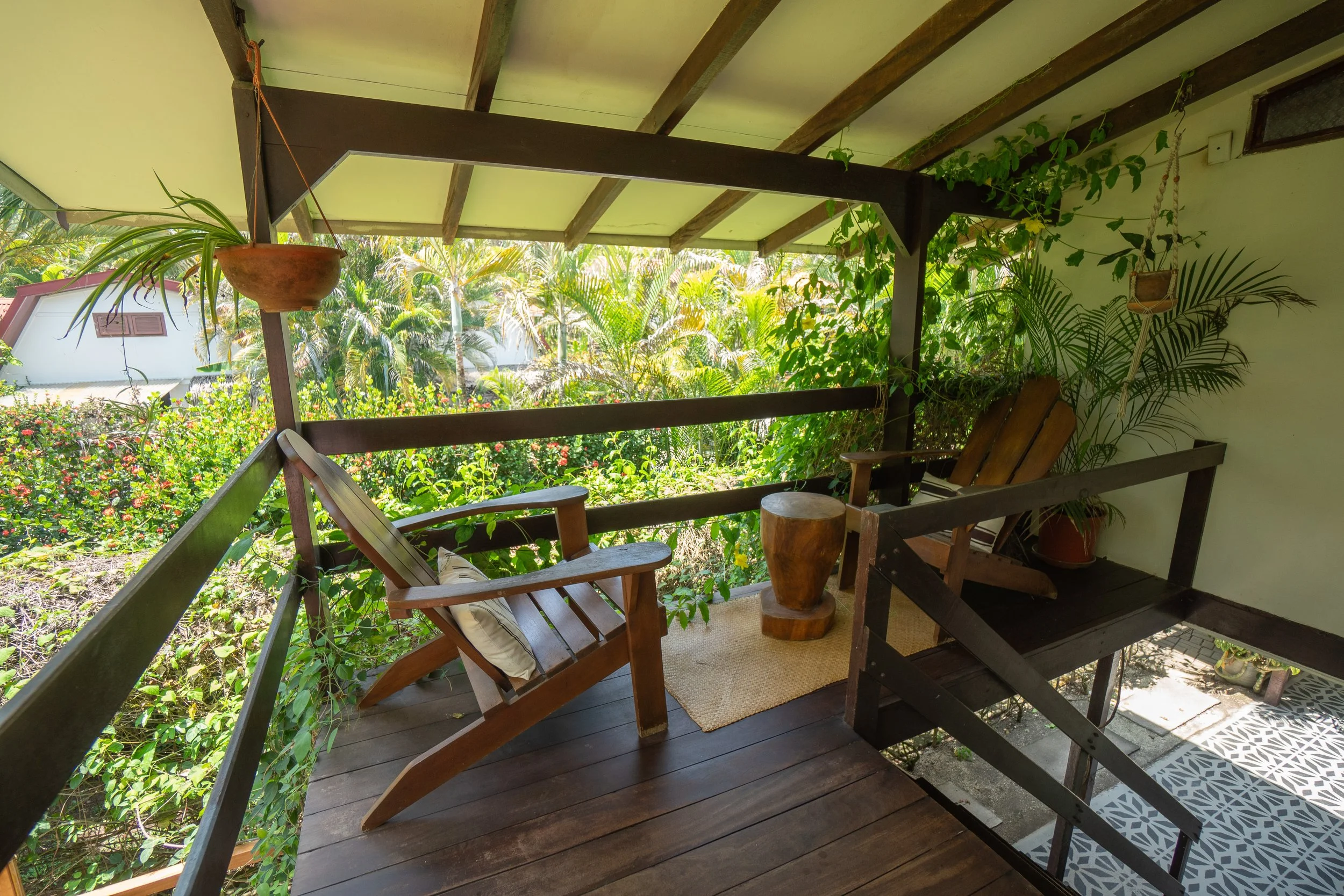 A cozy outdoor balcony with wooden furniture, surrounded by vibrant green plants and garden scenery.