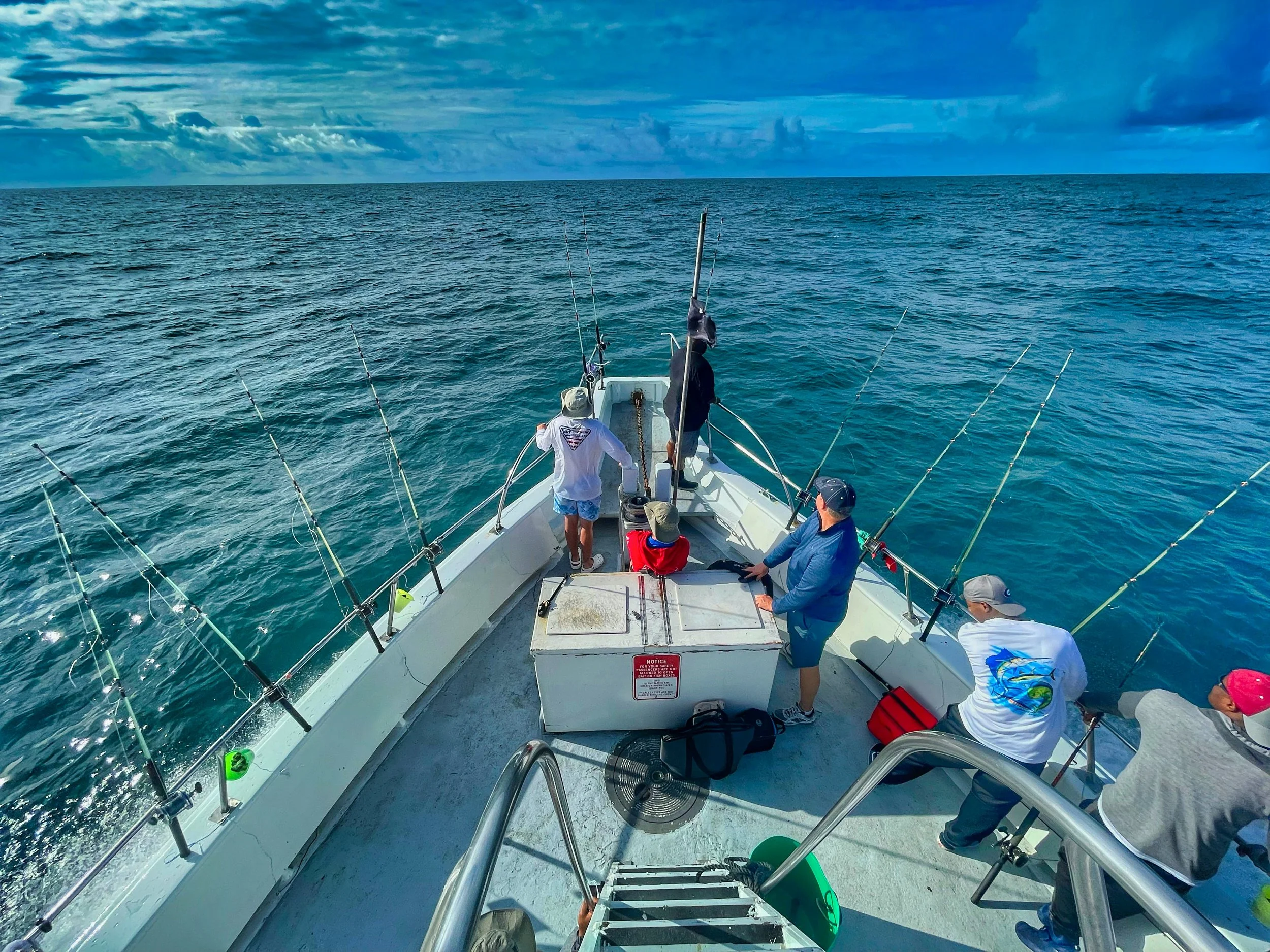 People fishing from a boat on the open water, with cloudy sky above.