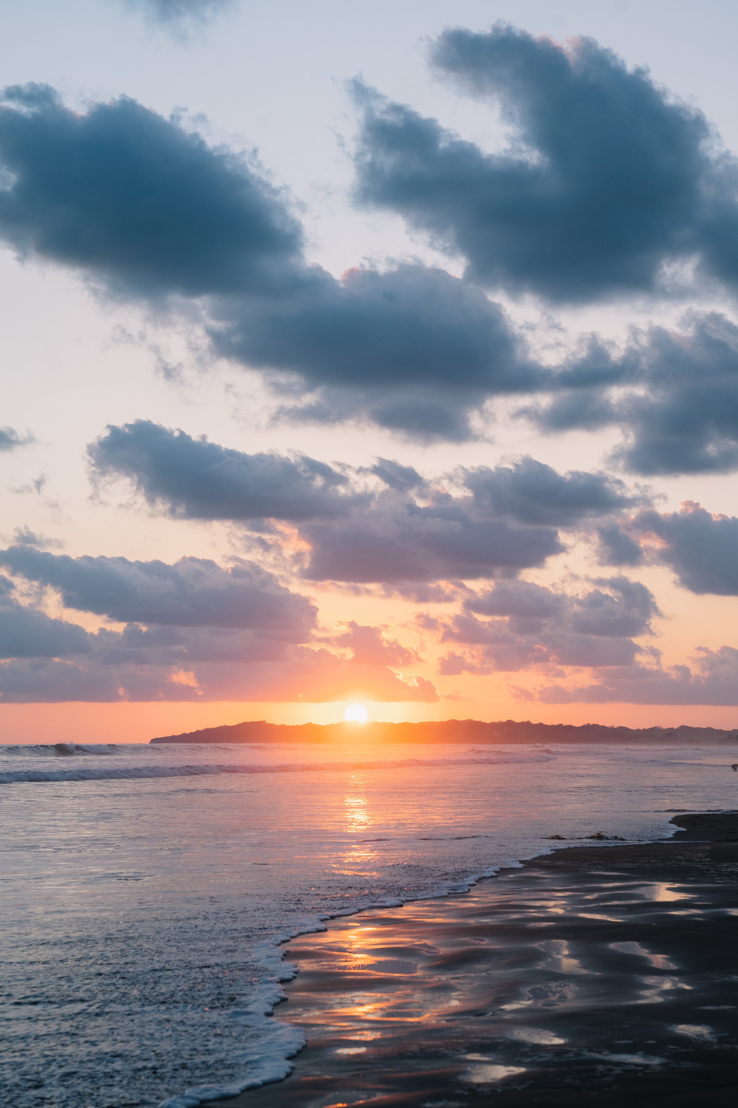 Sunset over the ocean with clouds in the sky and a small island in the distance.