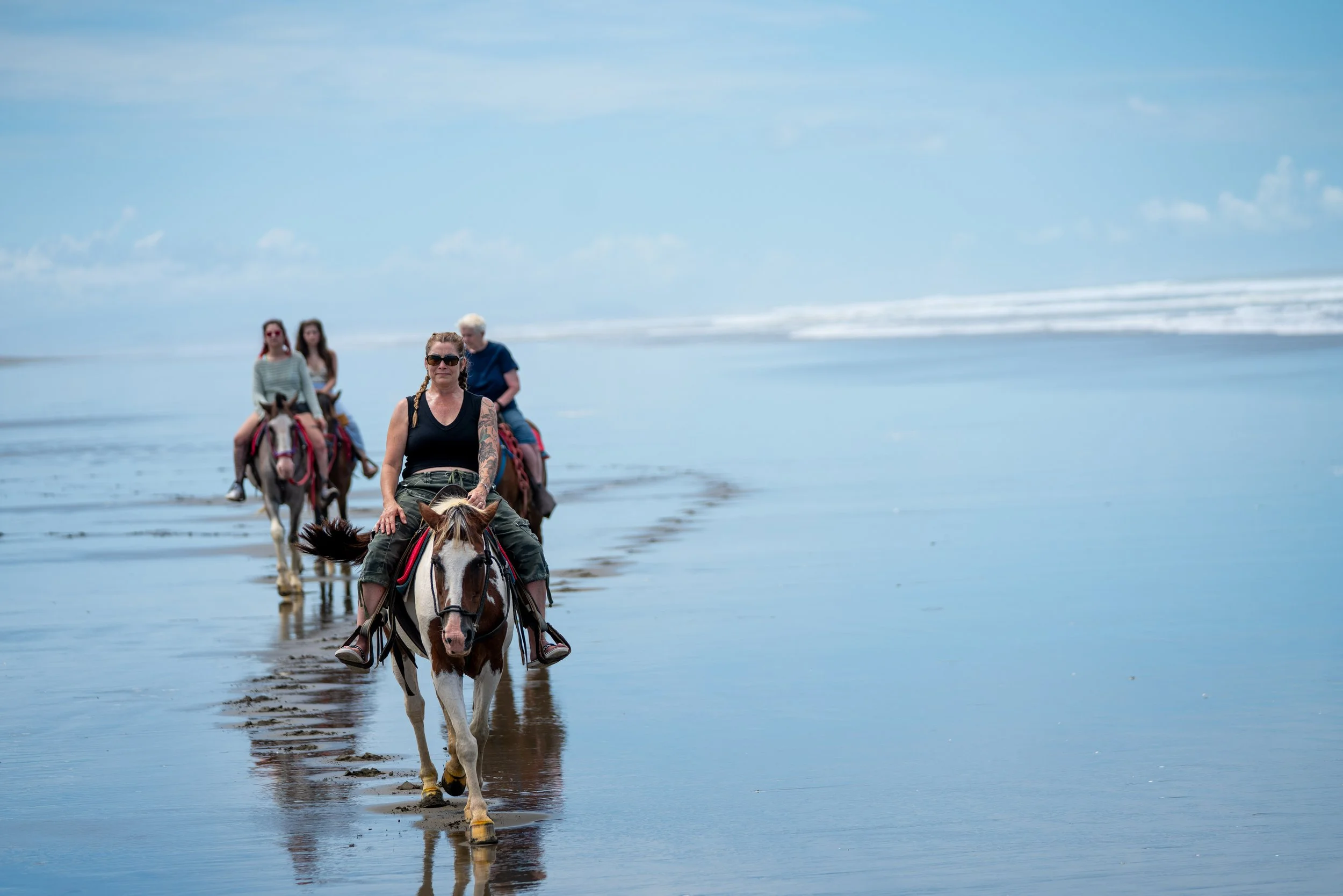 Group of people riding horses along the shoreline on a cloudy day.