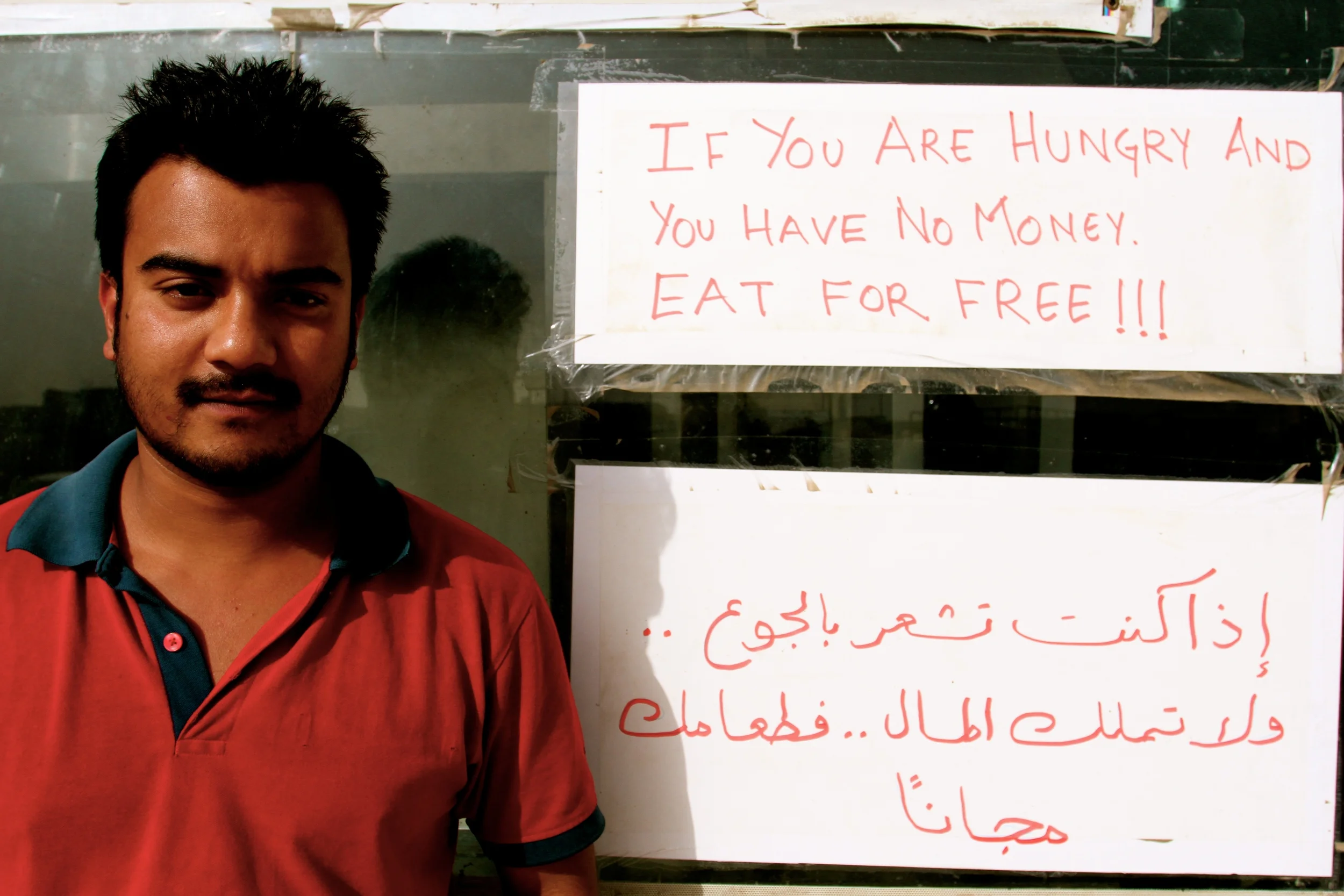 Zaiqa Restaurant manager Birkha from Nepal standing in front of the 'eat for free' sign.