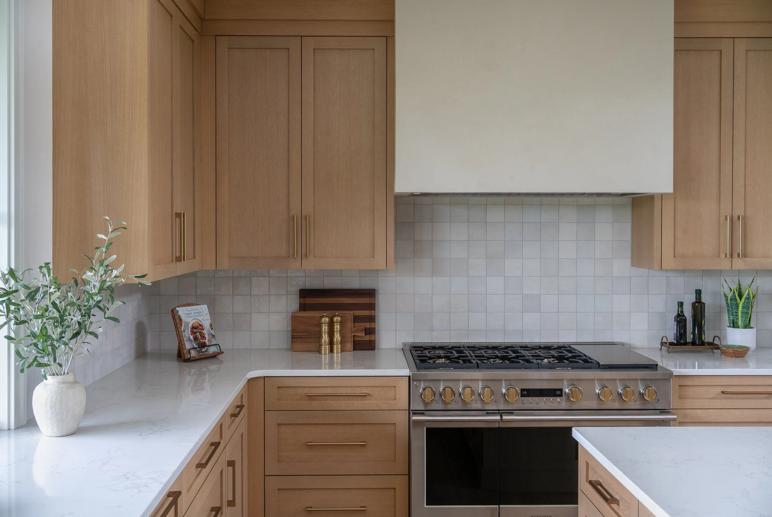Modern kitchen with light wood cabinets, white countertops, a stainless steel oven, and decorative plants and accessories.