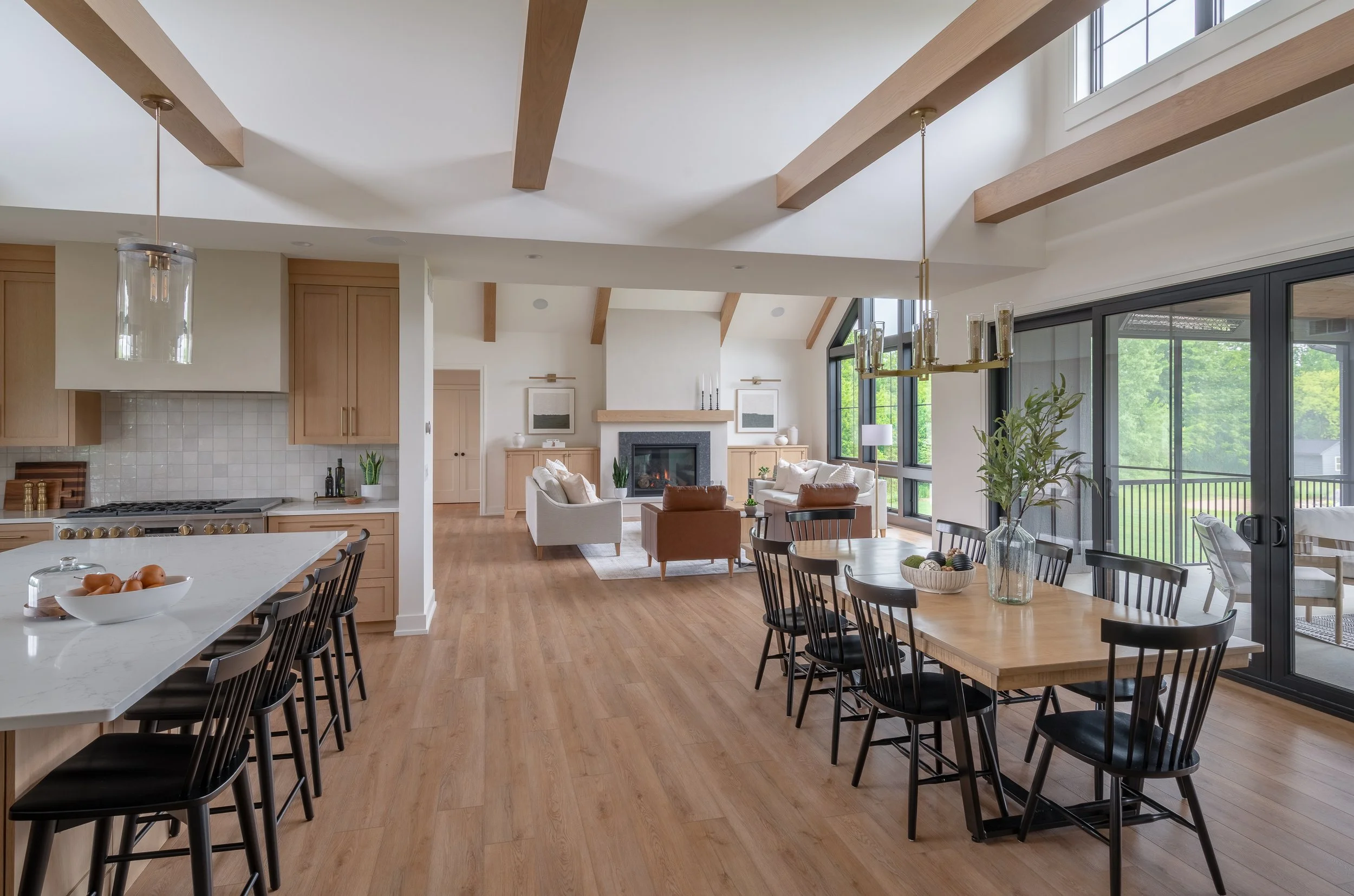 Open-concept living and dining area with wood floors, large windows, modern furniture, and a view of greenery outside.