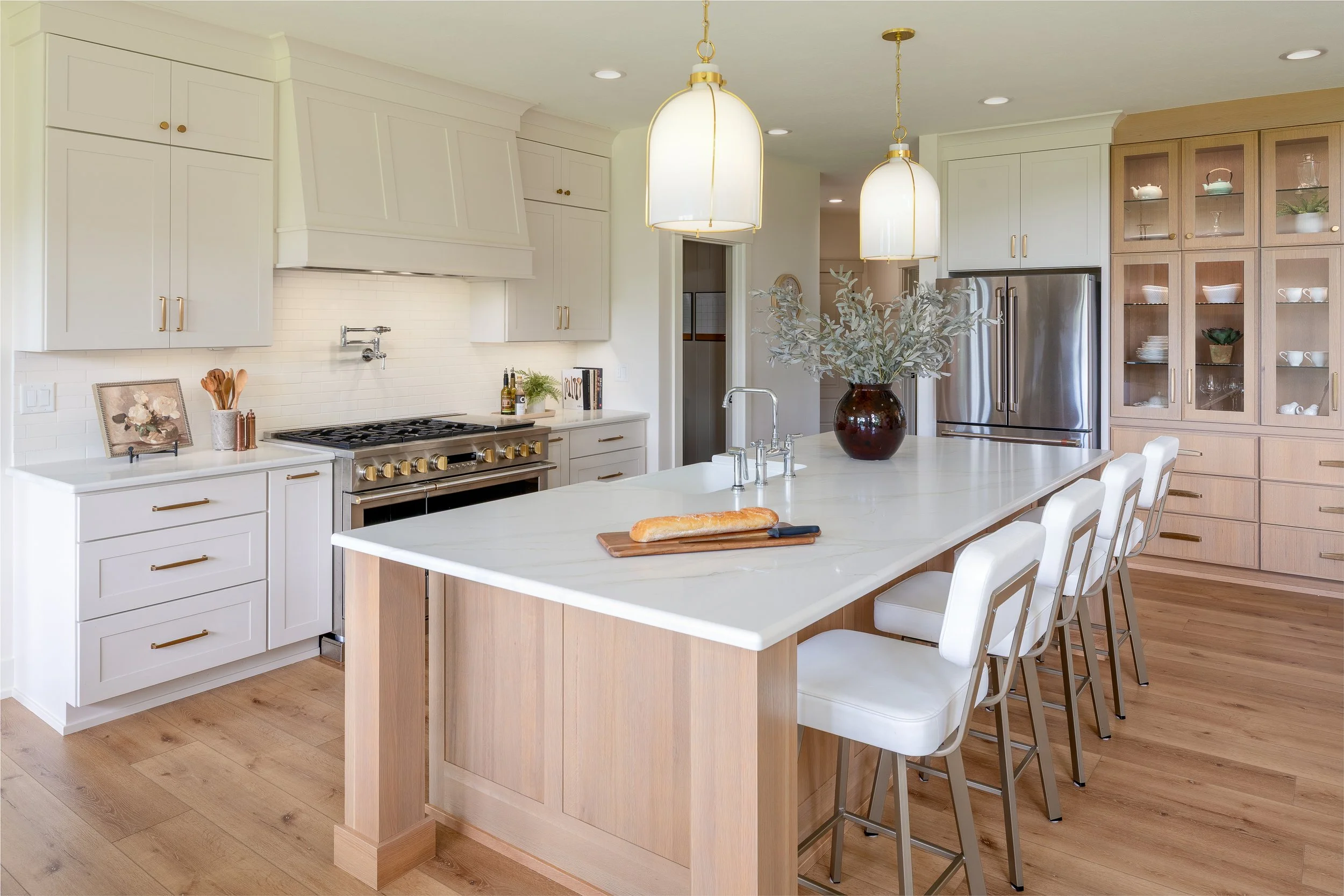 Bright modern kitchen with white cabinets, a large island with a marble countertop, a stainless steel refrigerator, and wooden flooring.