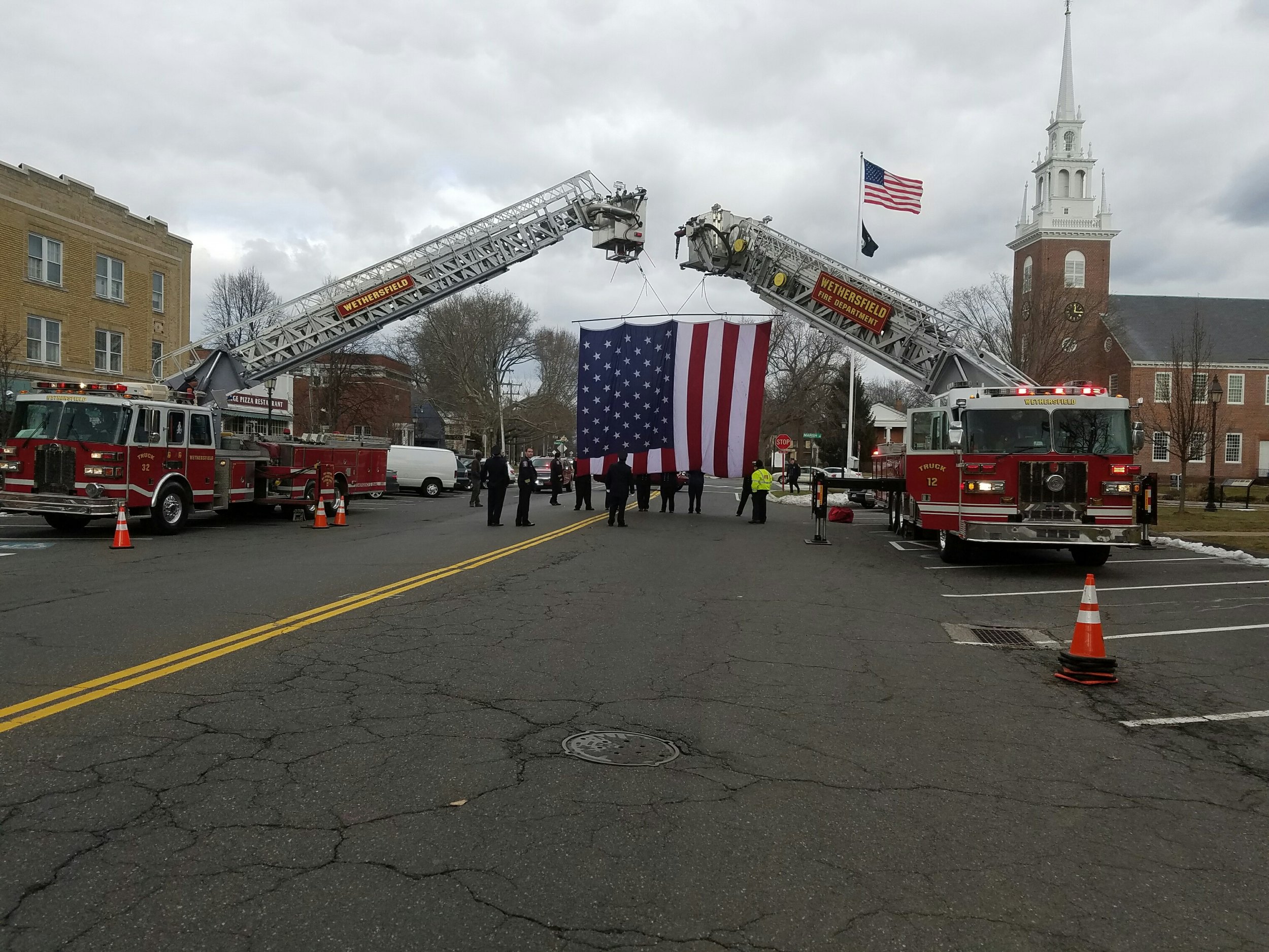 Firefighters begin raising the American Flag for the funeral procession of former Chief John McAuliffe.