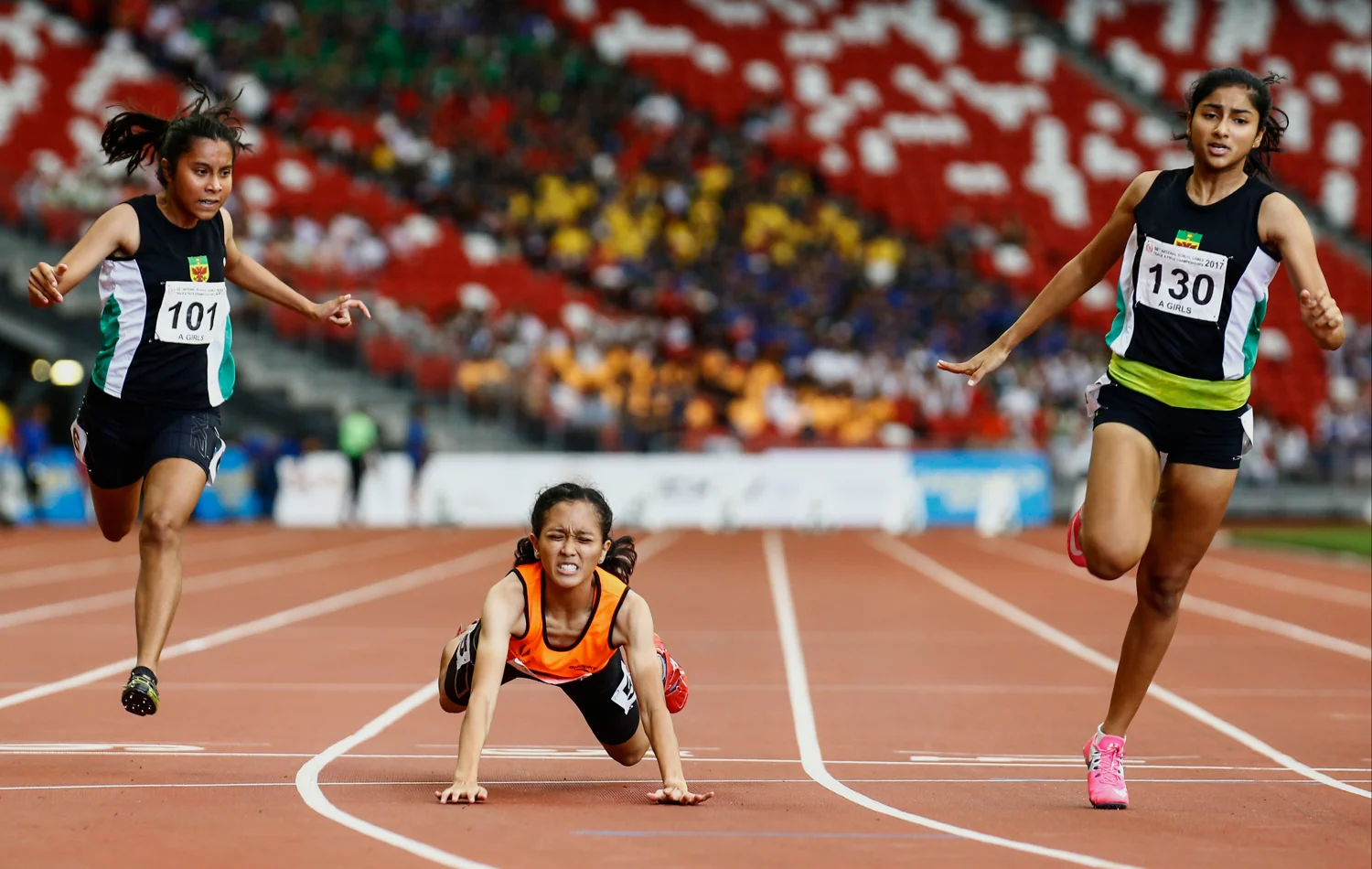 Tanisha Moghe (R) of Raffles Institution finishes in first place, while Ismi Zakiah (C) of Singapore Sports School stumbles at the finish line to finish second during the National Schools girls’ 'A' Division 100m final at the National Stadium on April 28, 2017 in Singapore.