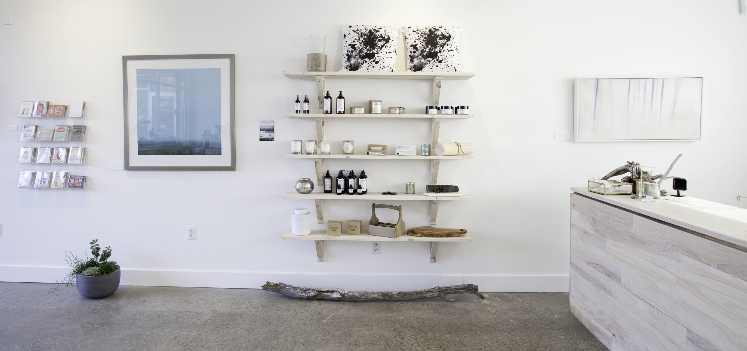 The east wall of the store, showcasing the shelving holding imported Swedish apothecary items and Linnéa candles together with other items for sale in my store. On the walls photography and greeting cards. To the right my custom-built checkout counter.