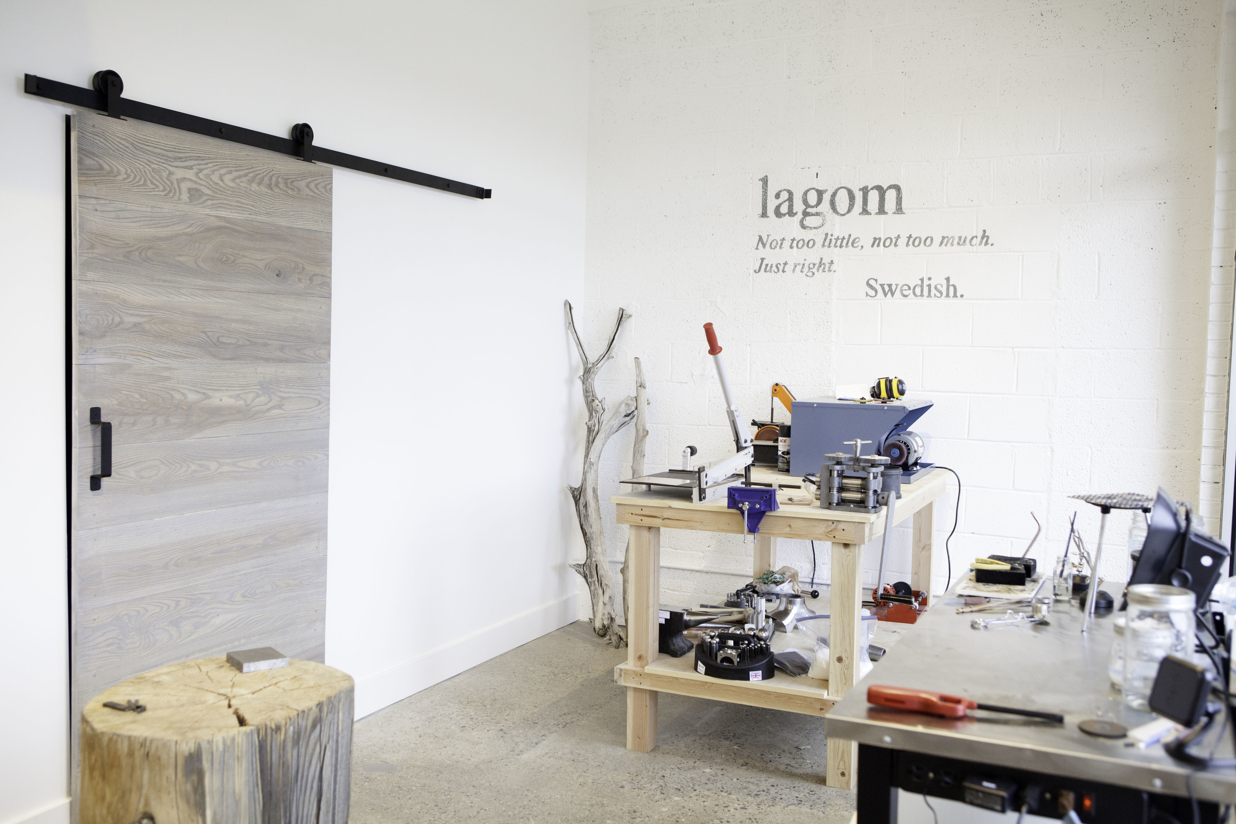 My open workshop. The stump I found in Idaho where I hammer, the workbench in the back that houses my many tools and machines, the soldering station to the right, the sliding barndoor that goes into my storage room and the hand painted Swedish saying of "Lagom" on the wall. 