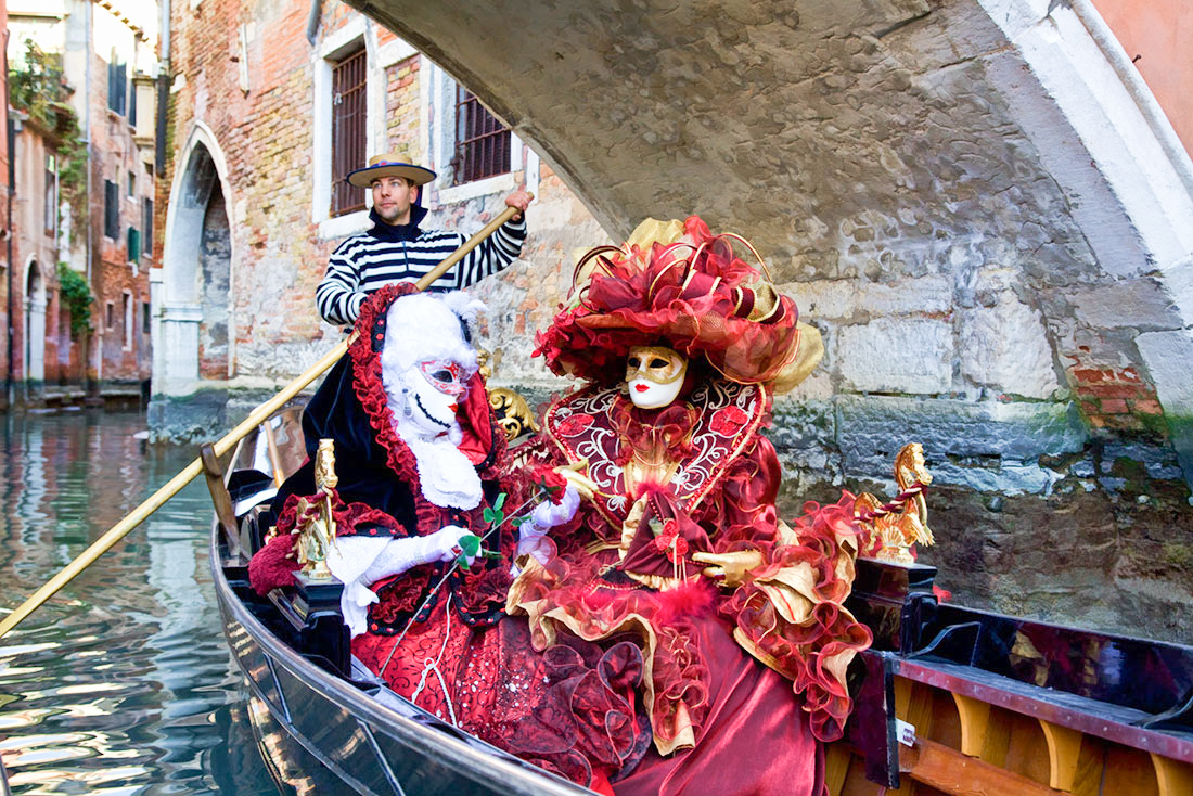 Women in elaborate Venetian masks and costumes enjoying a gondola ride during Carnival