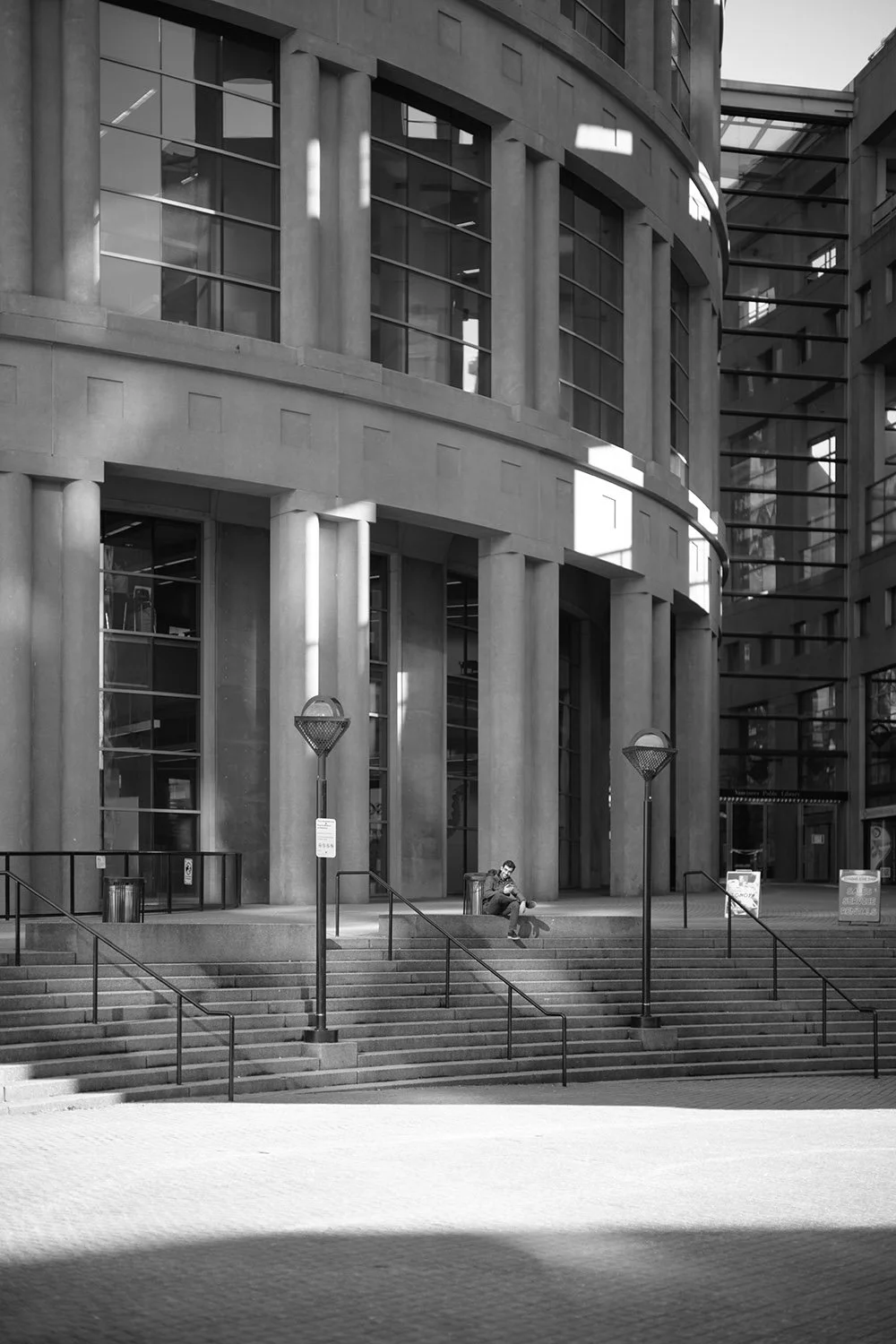 A man sits outside the Vancouver Public Library. Sample image from a Voigtländer Nokton 50mm f/1.2 Aspherical and Nikon Zf.