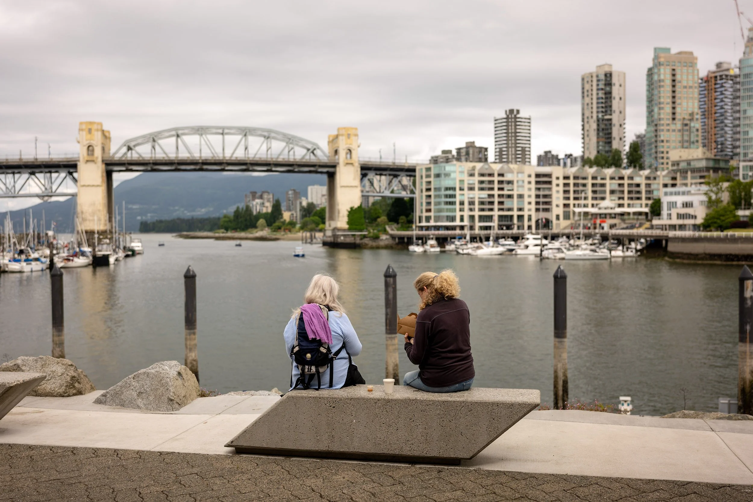 Two friends having lunch at Granville Island on grey June day, 2026