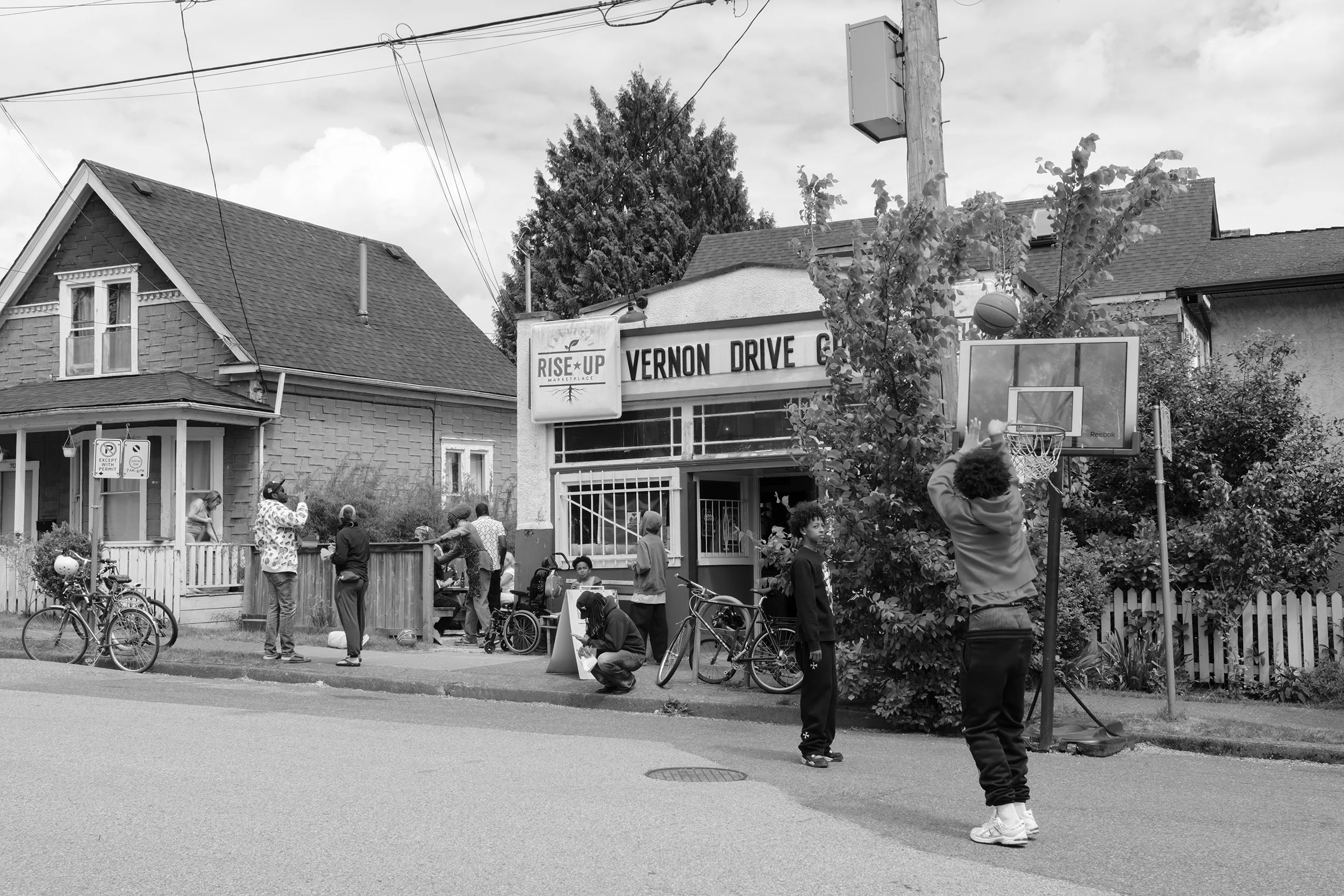 People hang out and kids play basket ball by the Vernon Drive Grocery Store in Vancouver. Sample image from a Fujifilm X-T50 and XF 16-50mm f/2.8 R LM WR.