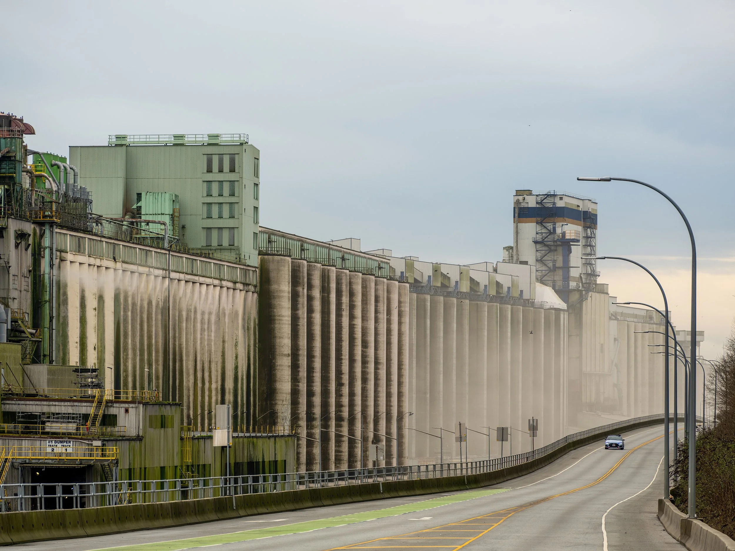 A car drives up Low Level Road in North Vancouver by the Cargill Grain Terminal. Sample image from a Fujifilm GFX 100S II and Fujifilm GF 100-200mm f/5.6 R LM OIS WR