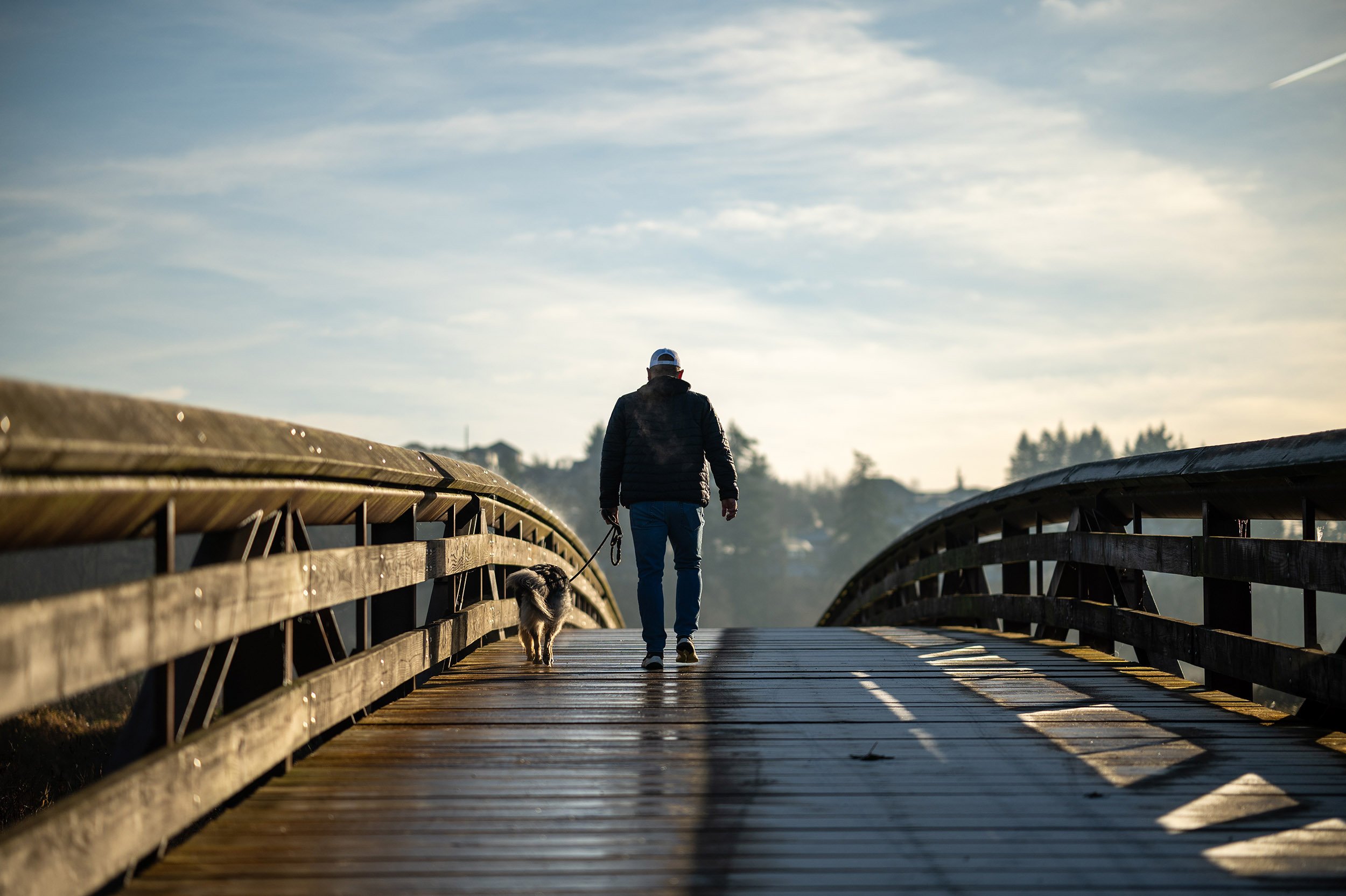 A man walks his dog across a bridge on the Coquitlam River. Tree and reflection, Coquitlam River. Sample image from a Viltrox 56mm f/1.2 Z (Nikon Z-Mount) and Nikon Z8.